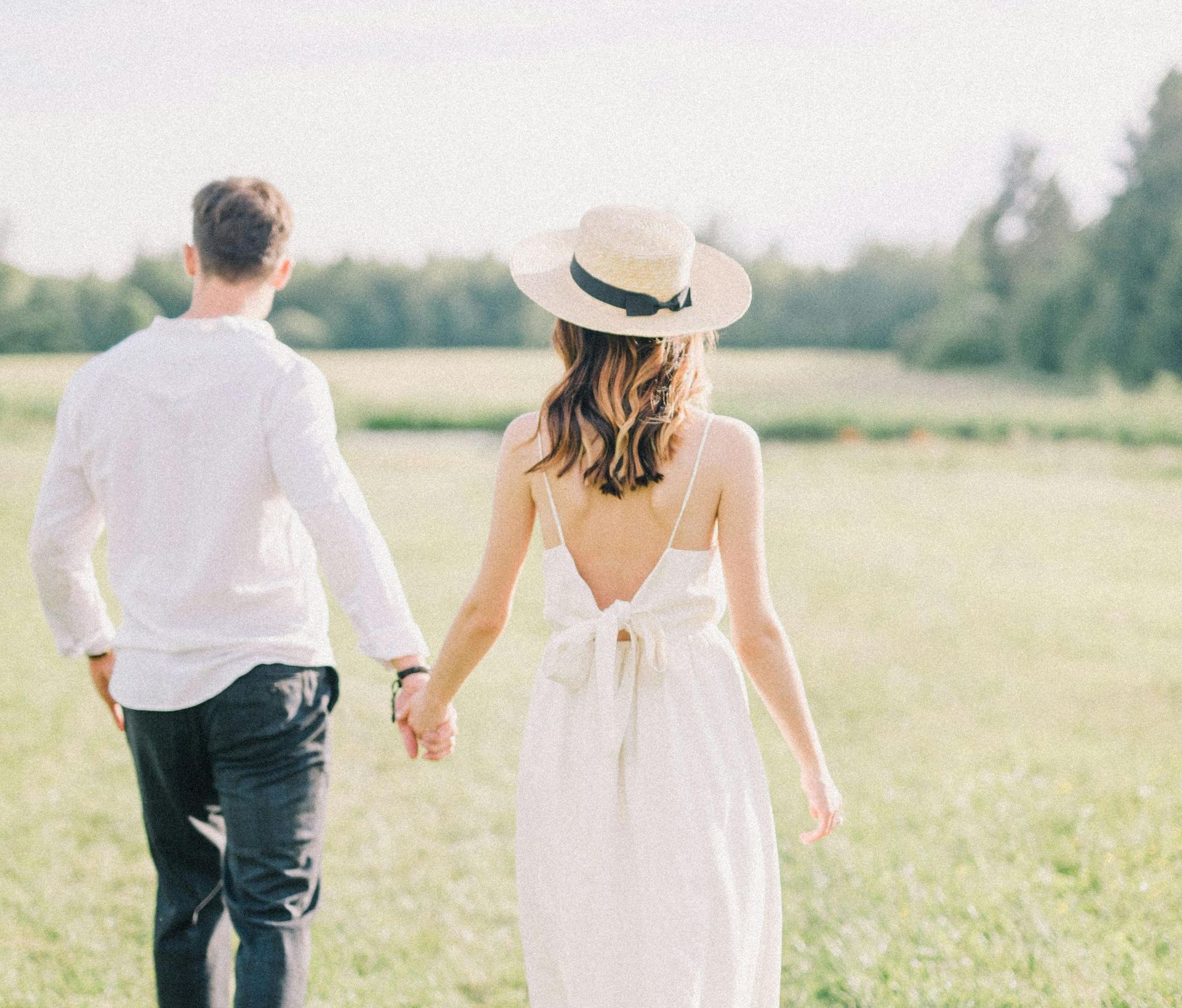 A man and a woman are walking through a field holding hands.