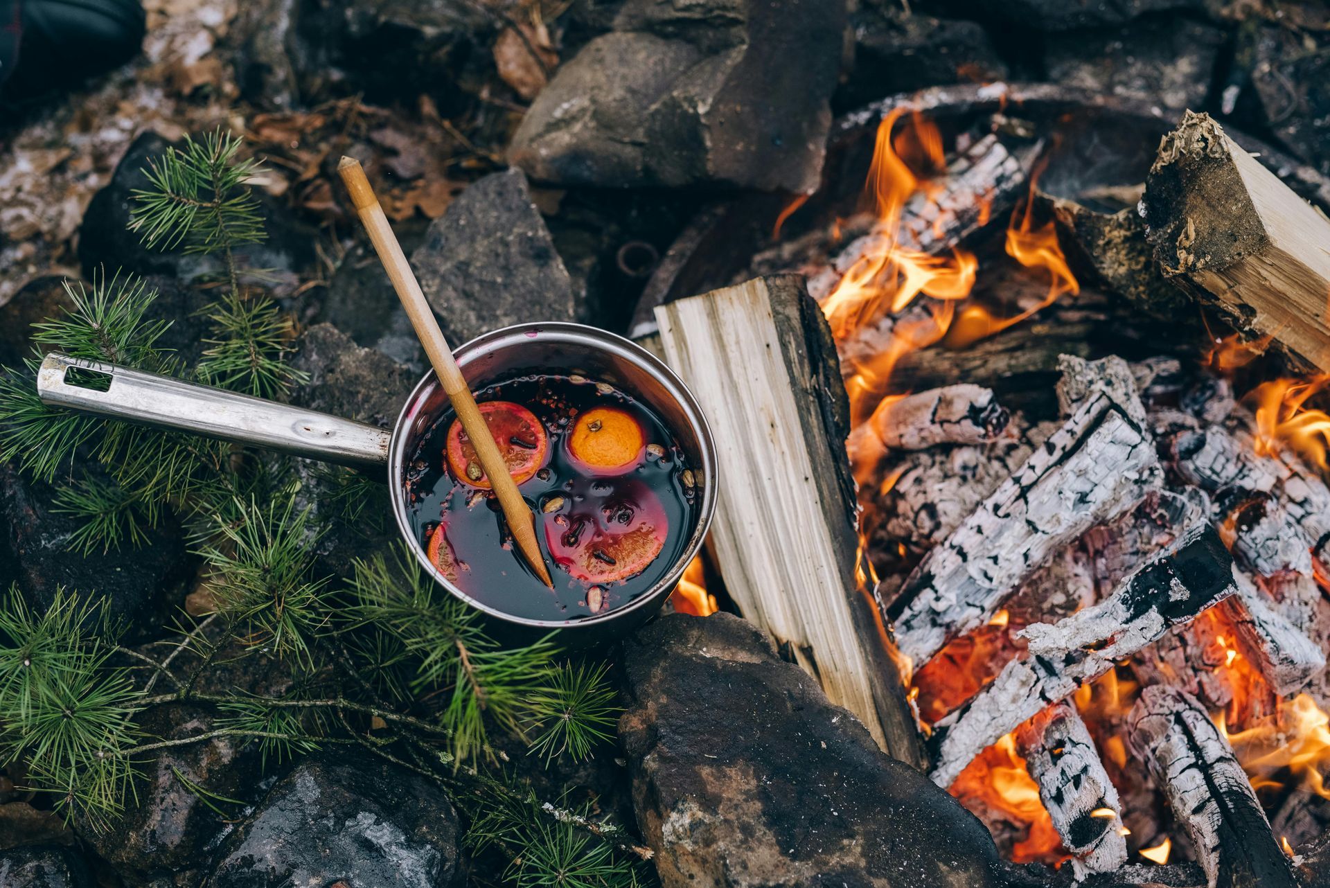 Pot of mulled wine with fruit, on a fire pit with burning wood.