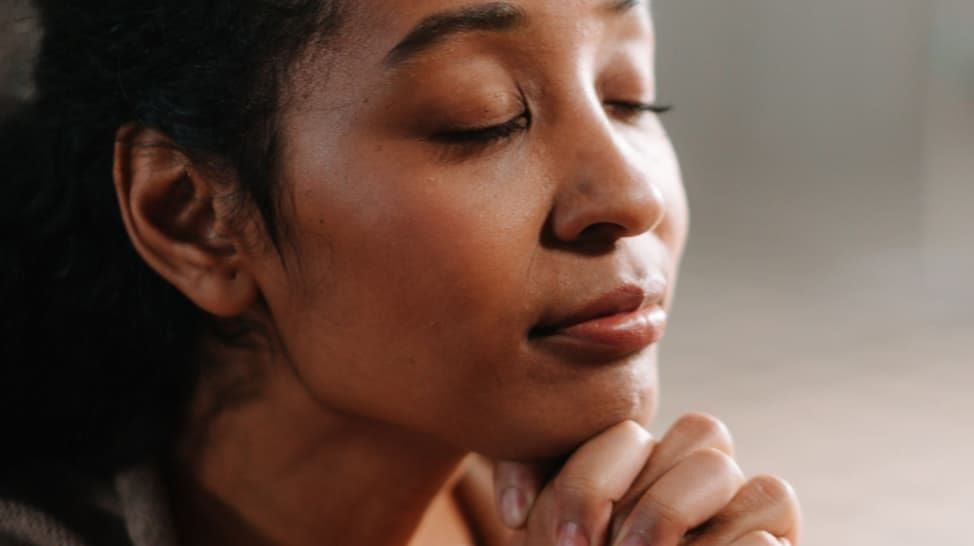 Woman with closed eyes and hands clasped in prayer.