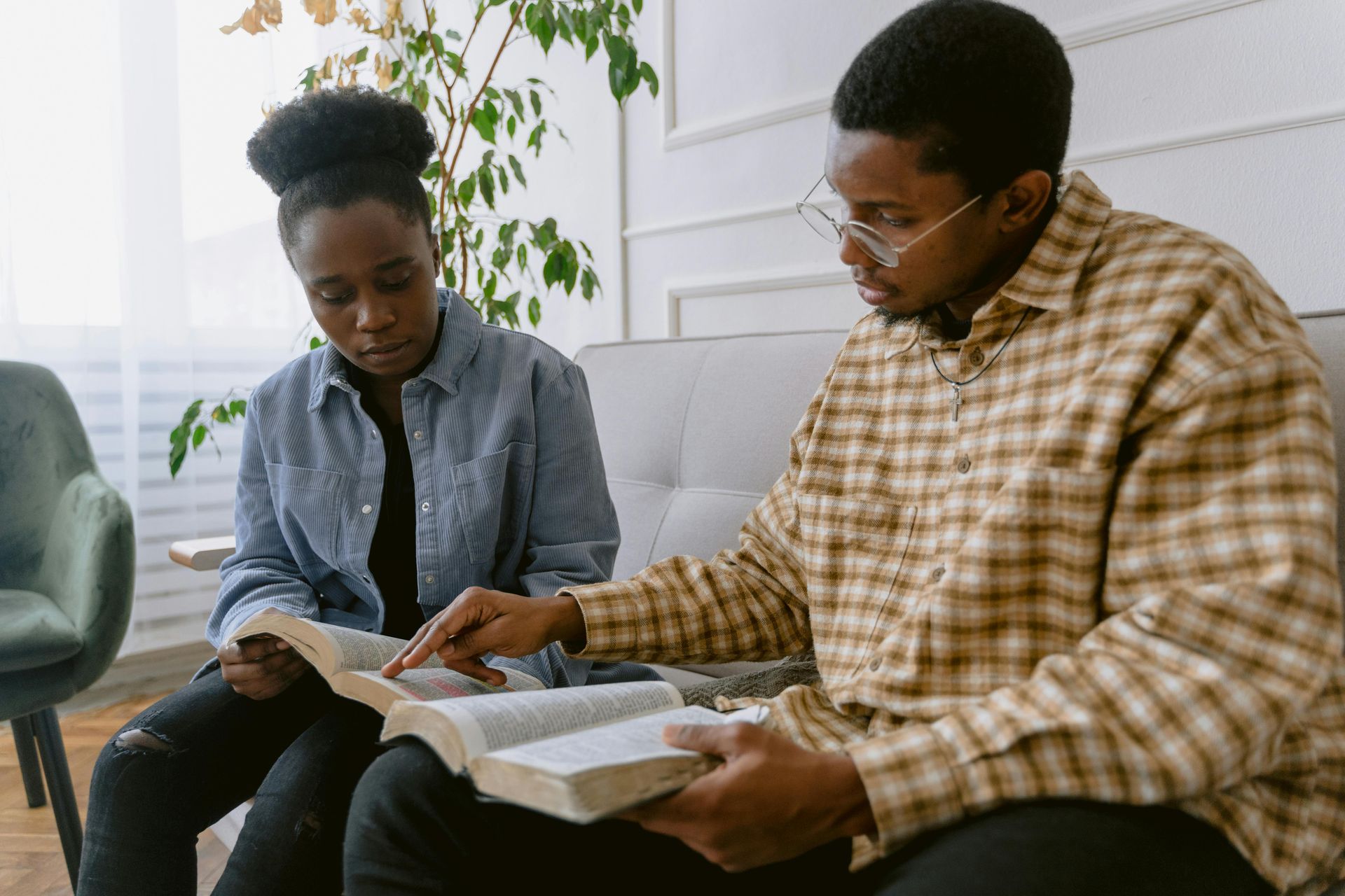 Two Black individuals sitting, reading a book together; the man points to the pages.