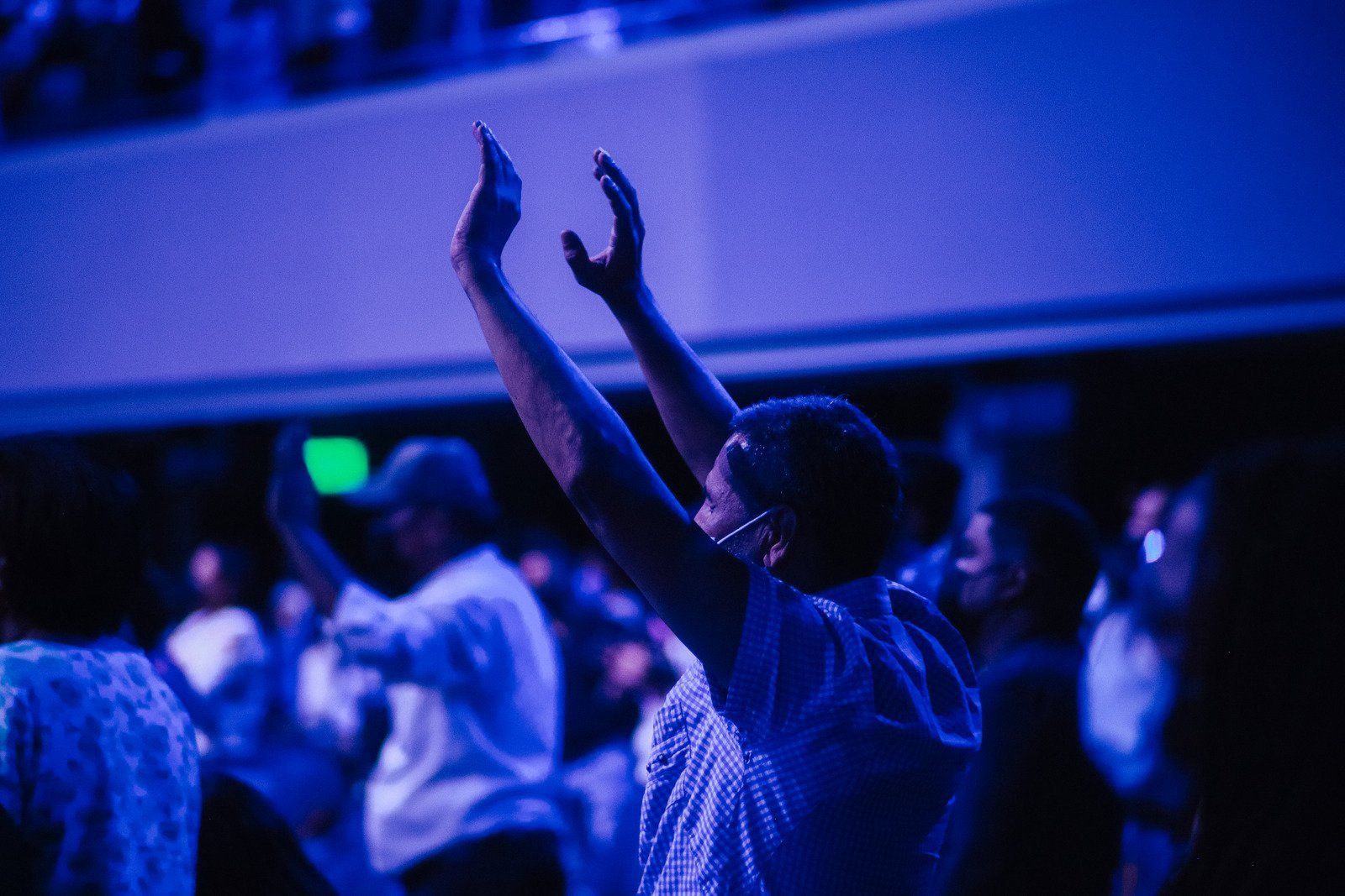 Person raising arms in worship with a crowd in a blue-lit church.