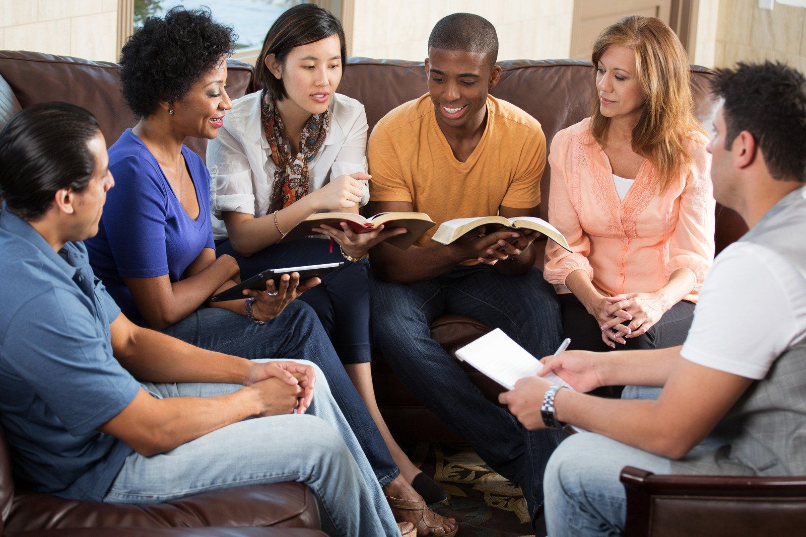 Group of diverse people seated on a couch, reading books and interacting.