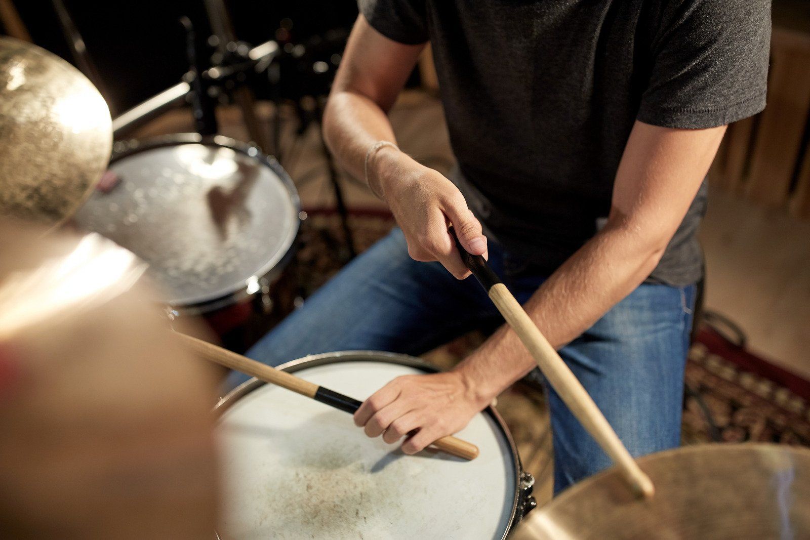 Drummer playing a drum kit, hands holding sticks, blurred background.