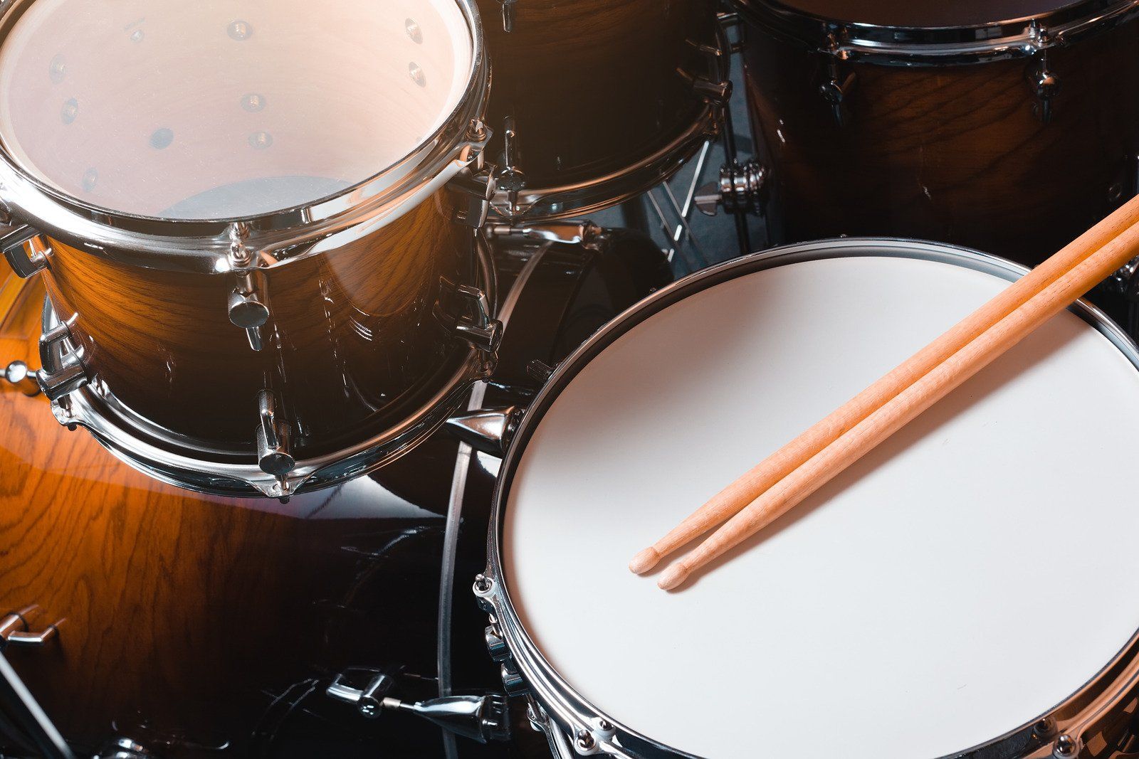 Drums with wooden sticks resting on a white drum. Dark wood finish.