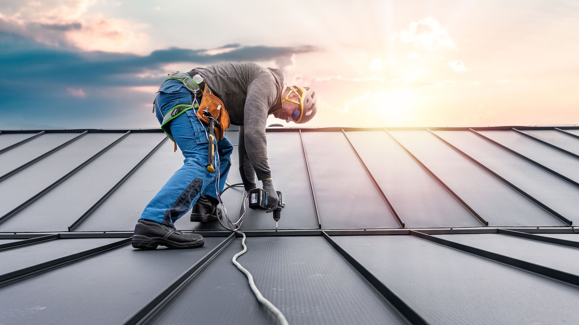 A man is working on a roof with a drill.
