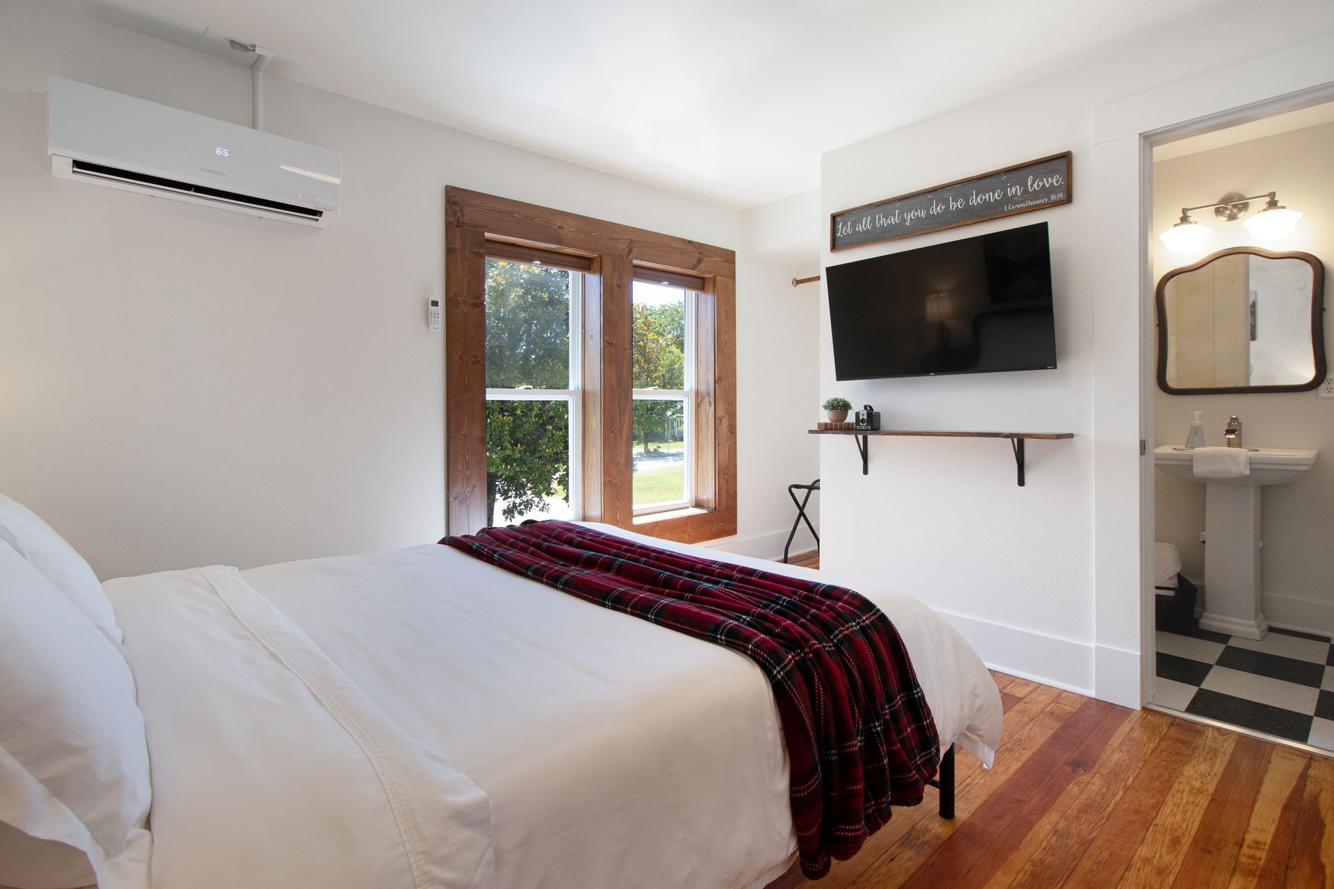 A bedroom with a bed , television , air conditioner and a sink.