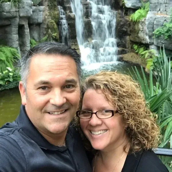 A man and a woman are posing for a picture in front of a waterfall.