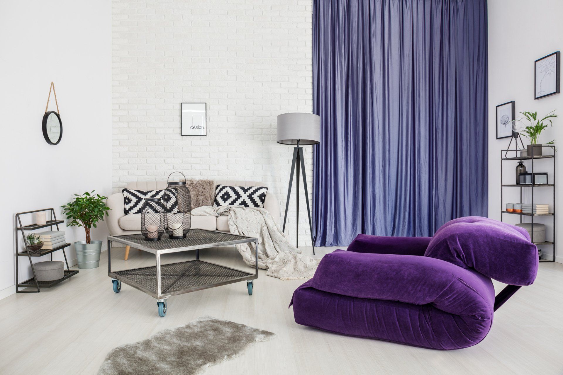 White plaster and brick walls in industrial setting lounge. Industrial trolley coffee table, shelves and lamp. Brigh purple plush lounge chair in front of closed purple curtains.