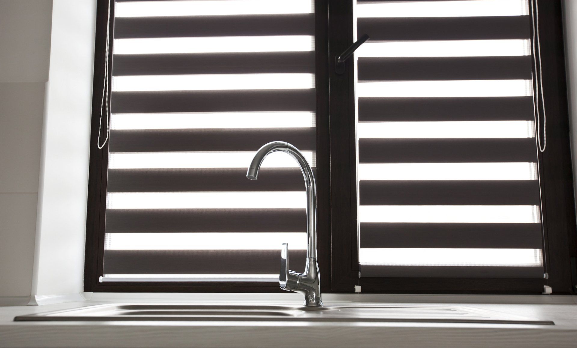Dark plantation shutters, opened over kitchen sink and bench with chrome mixed tap.