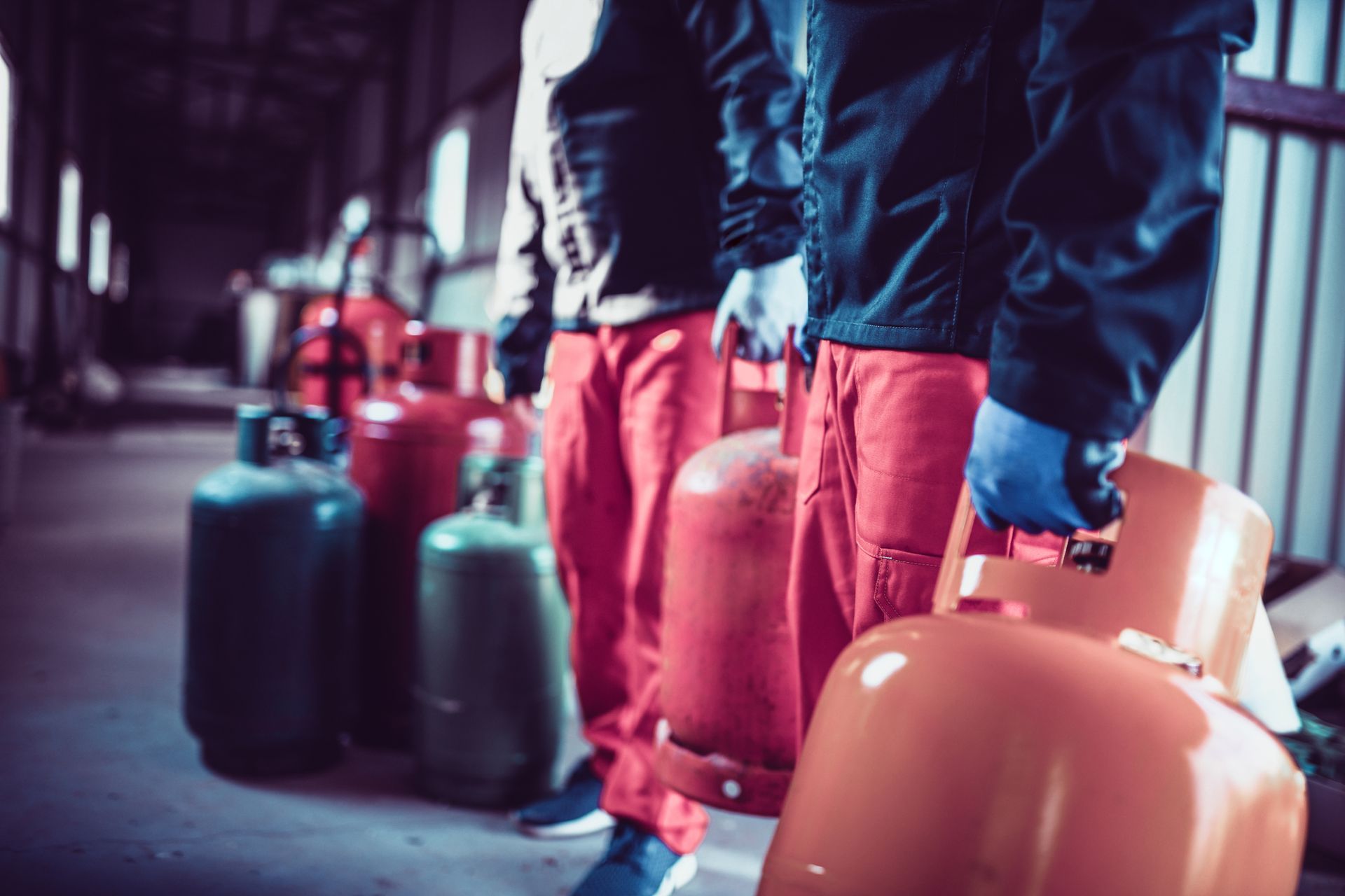 Two men wearing black jackets and gloves are positioned next to propane gas tanks in a storage area.