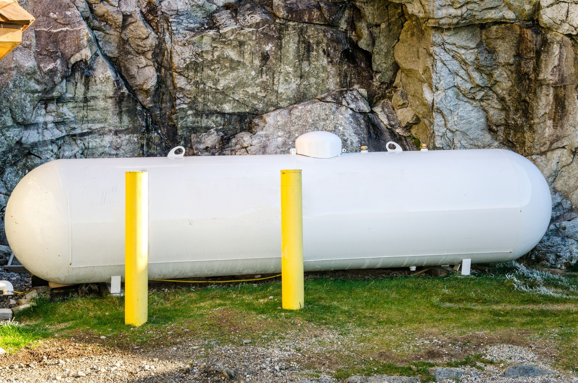 White propane tank in the outdoors, laying on the grass and in front of a cave.