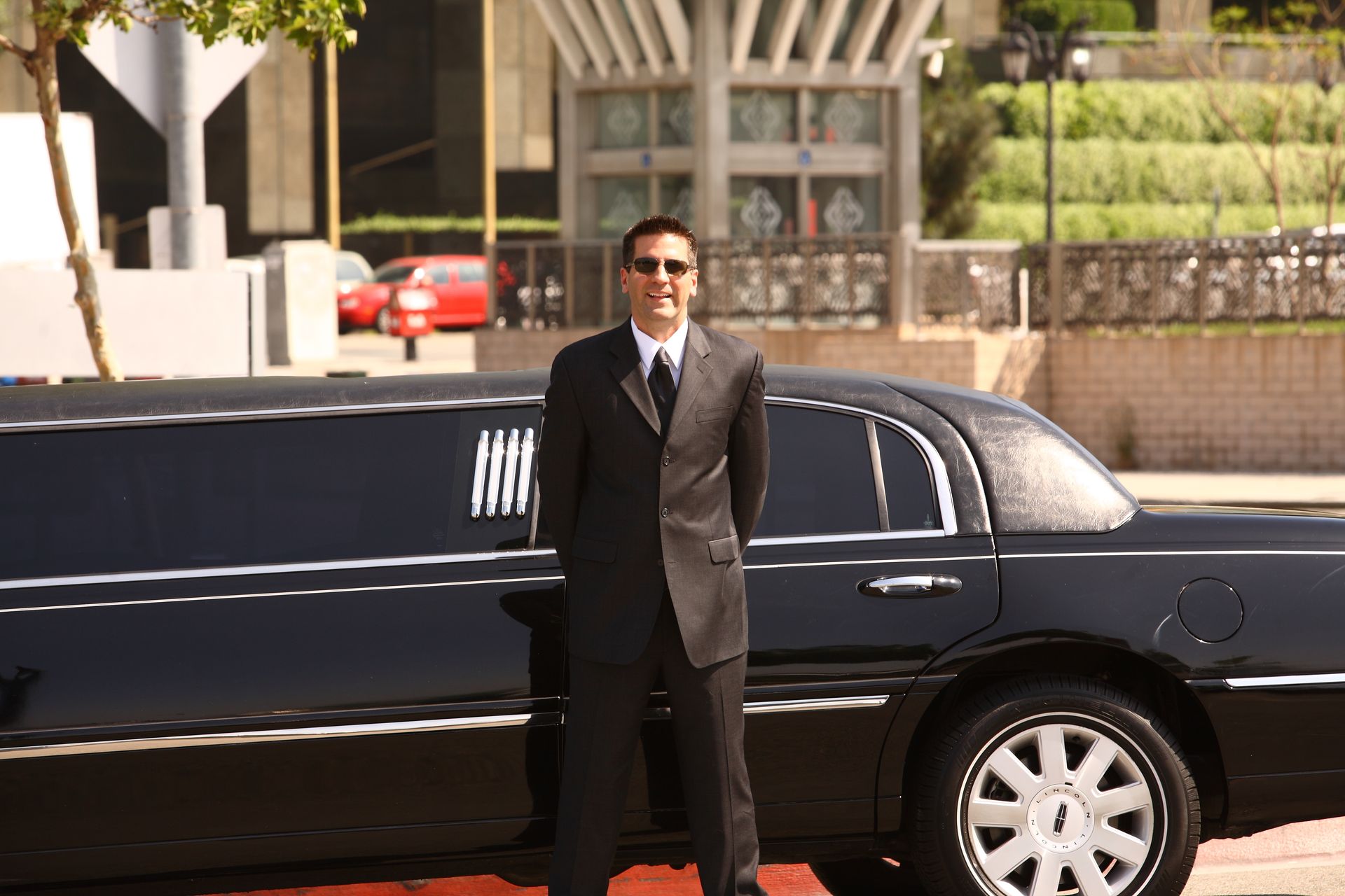 Man in suit and sunglasses stands in front of a black limousine