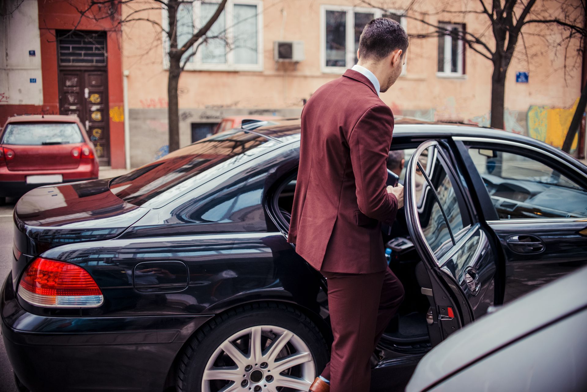 Man in maroon suit exiting a black car