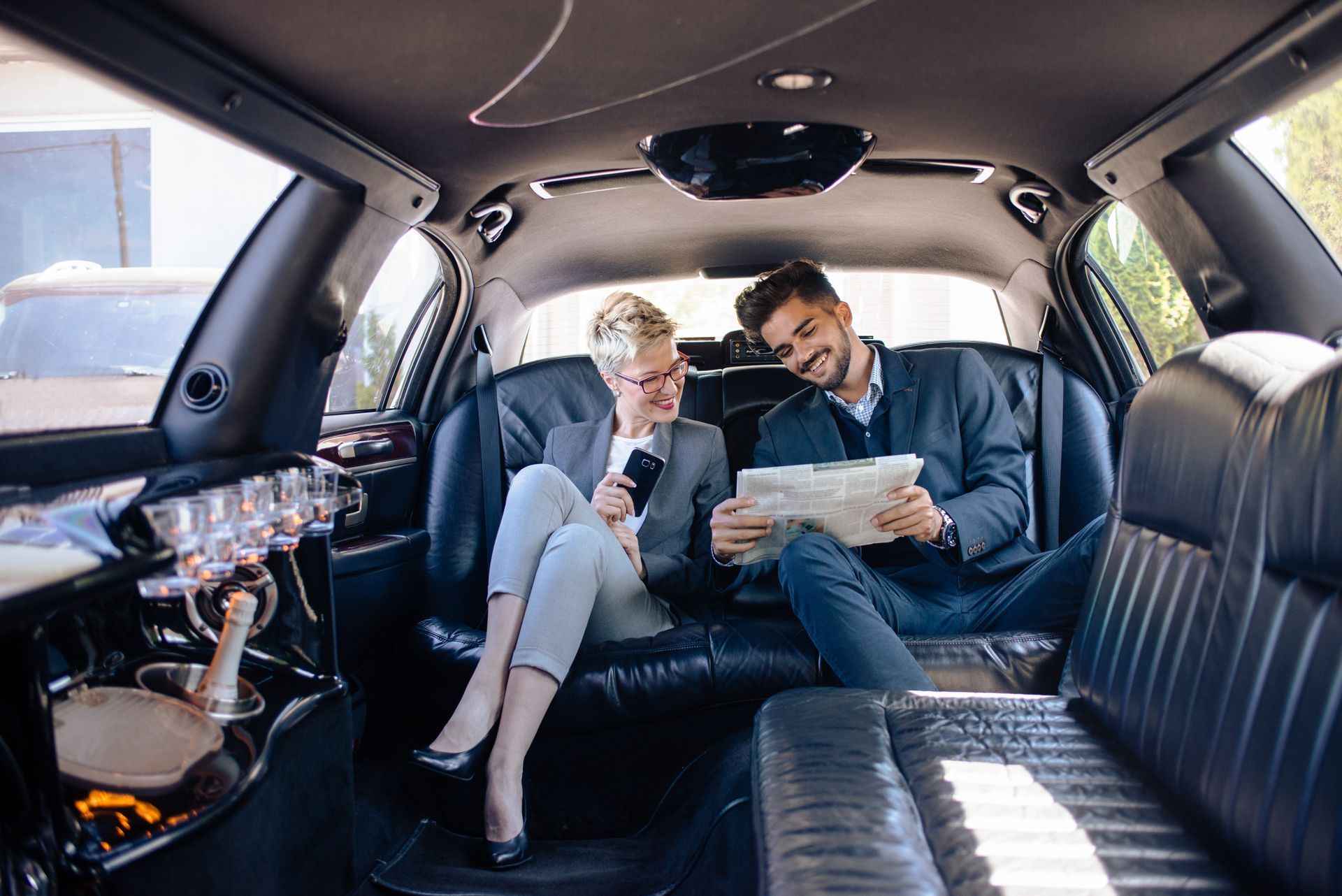 Inside a limousine, a person on a phone and a man reading a paper