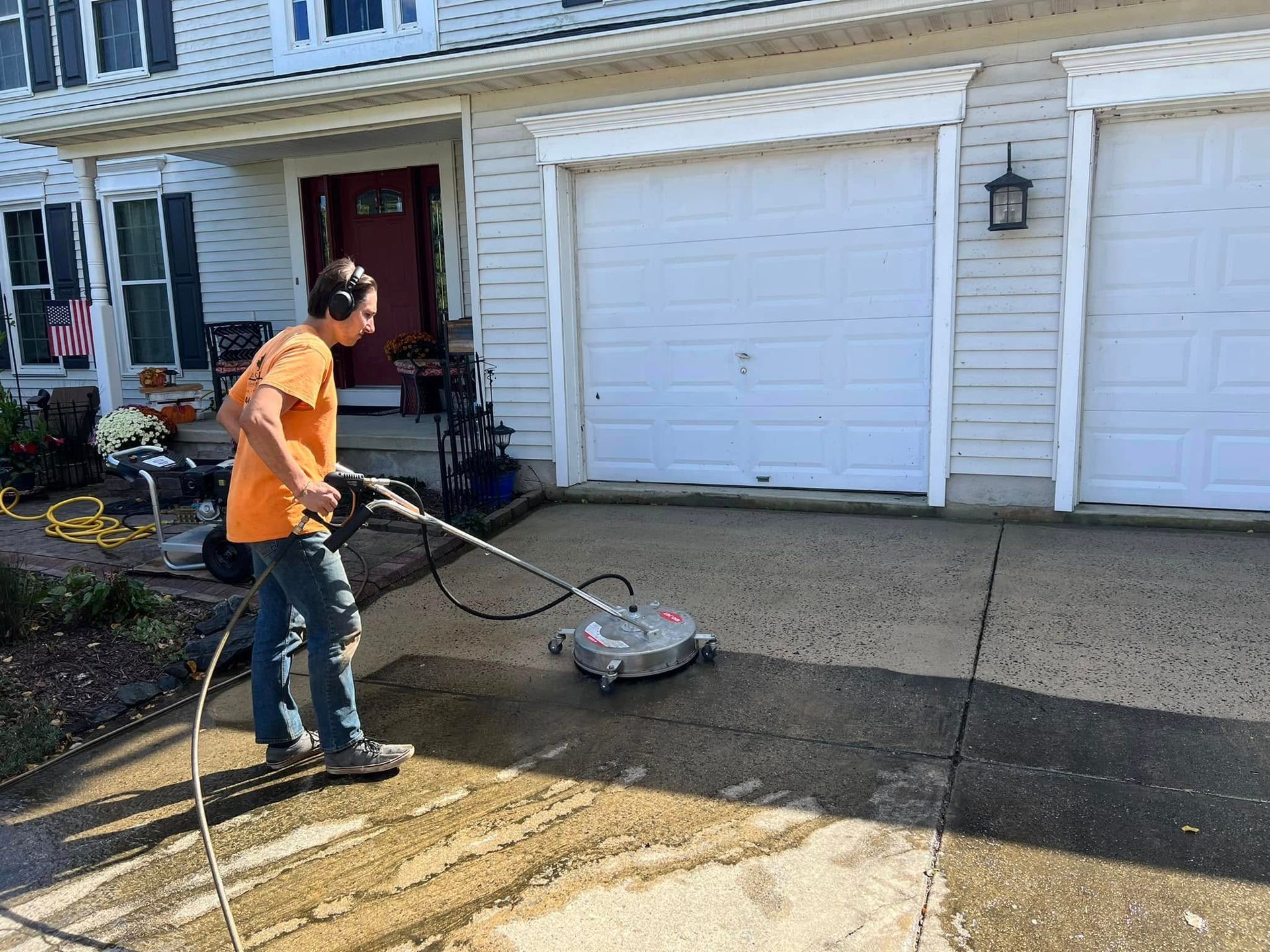 A man is using a pressure washer to clean a driveway in front of a house.