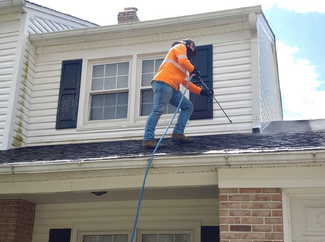 A man is cleaning the roof of a house with a pressure washer.