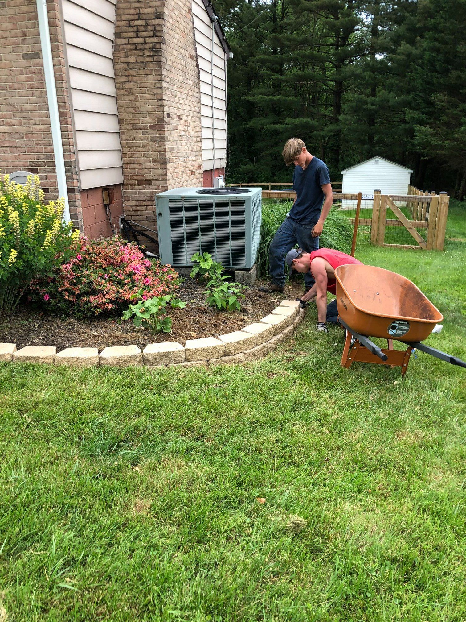 A man is pushing a wheelbarrow in a yard next to a house.