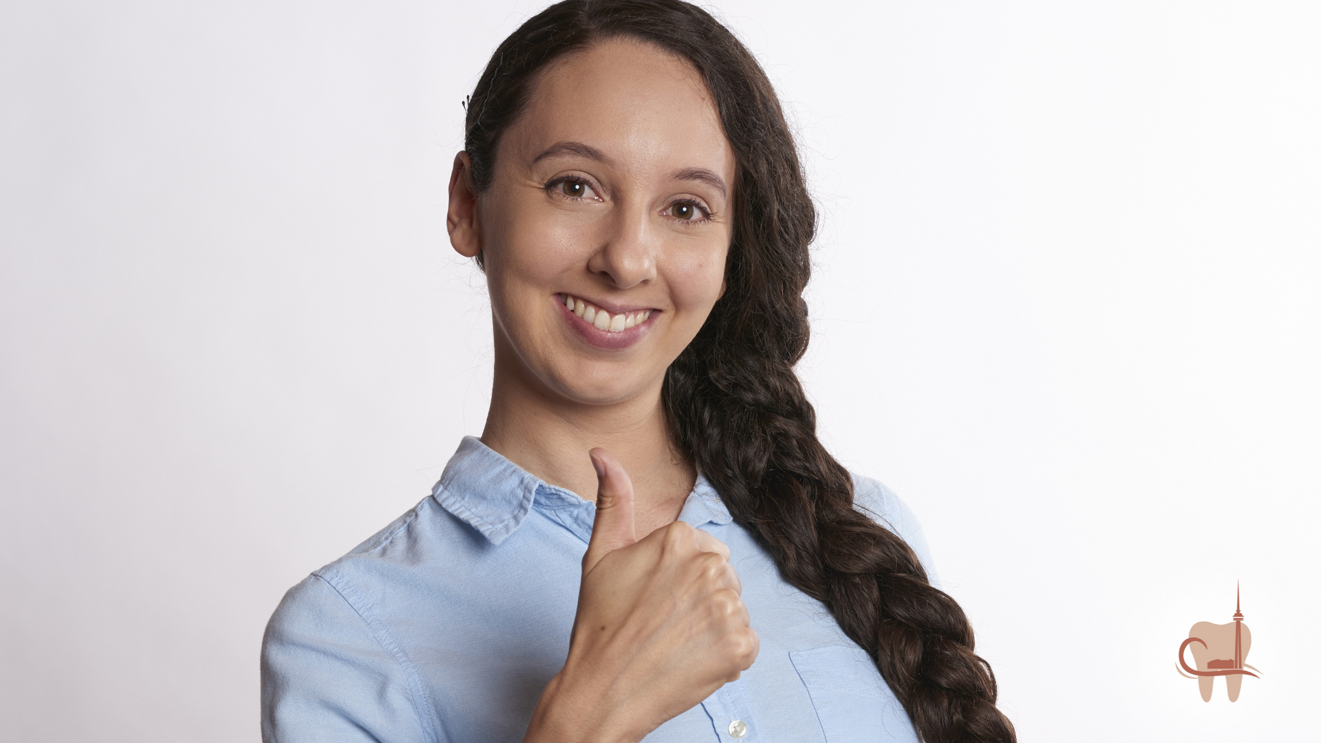 Woman with long brown hair, smiling, giving thumbs up, wearing blue shirt.