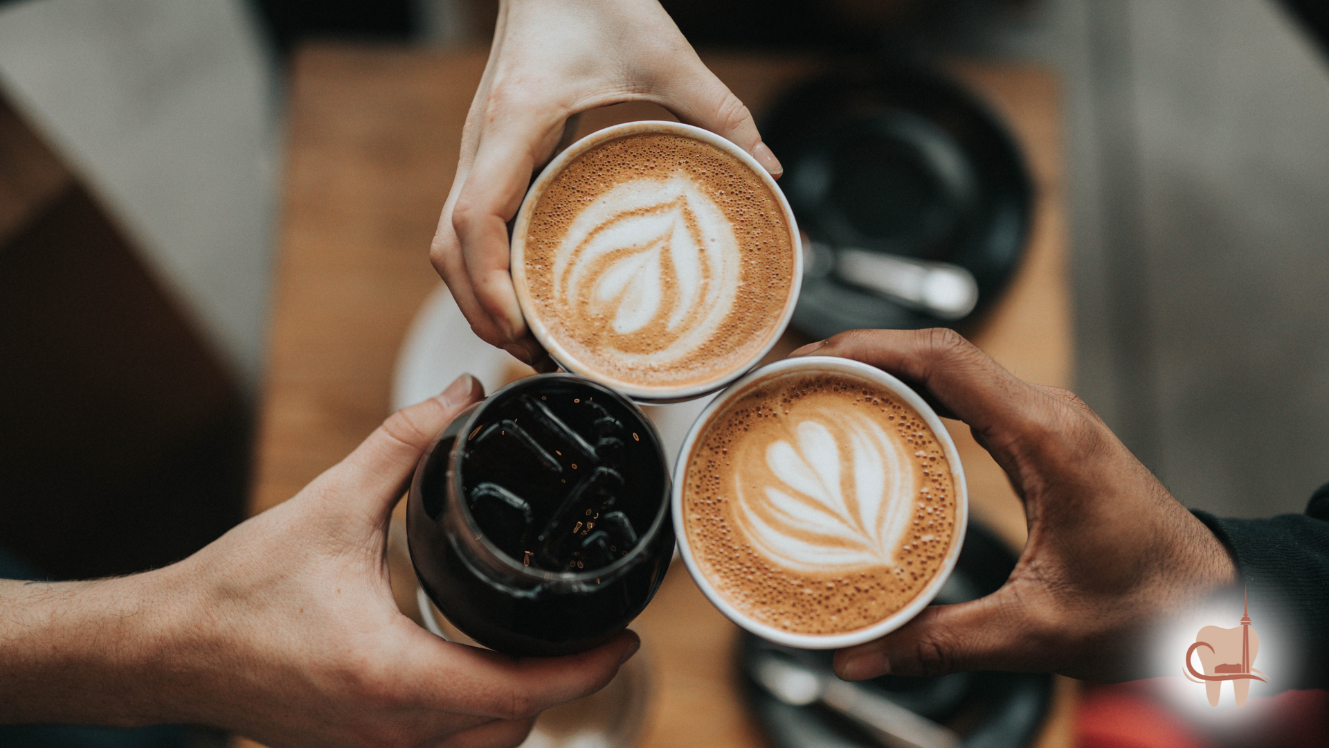 Three people holding coffee cups together, two lattes with latte art and one iced coffee.