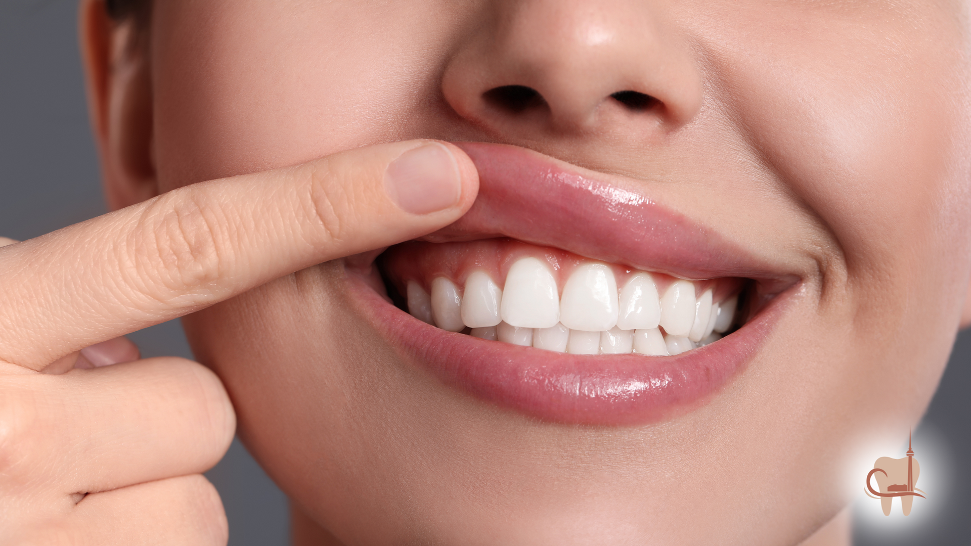 Woman smiling, pointing to her white teeth and full, pink lips.