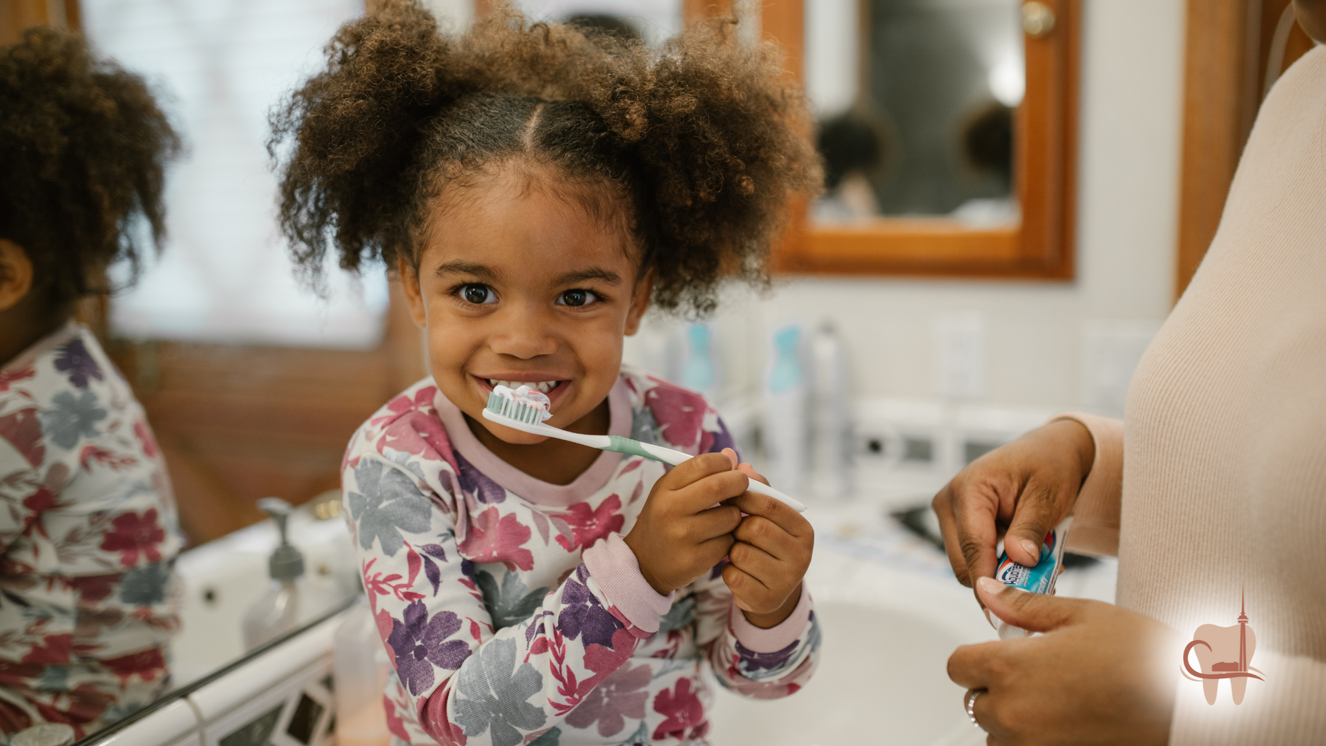 Smiling Black girl brushing teeth with mother in bathroom.
