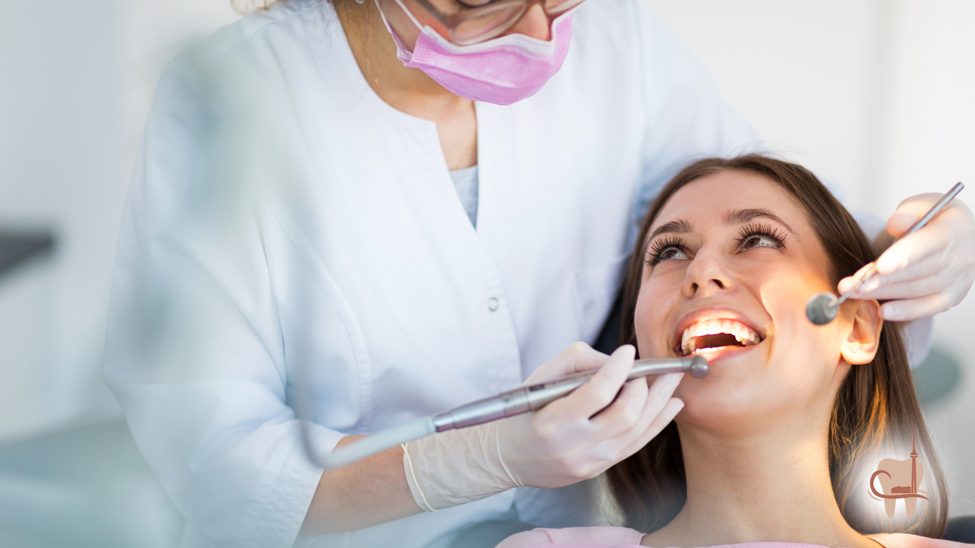 Dentist examining patient's teeth in a clinic, using tools. Both are smiling, dressed in professional attire.