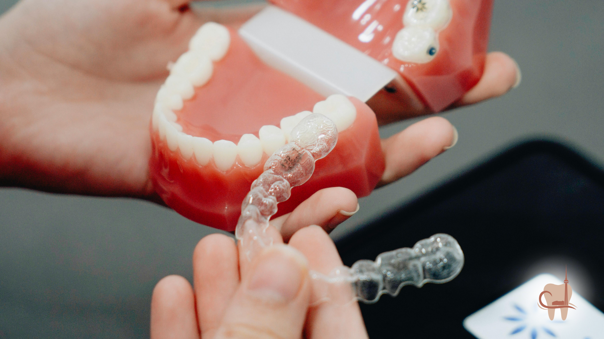 Person holding clear aligners near a model of teeth; close-up shot.