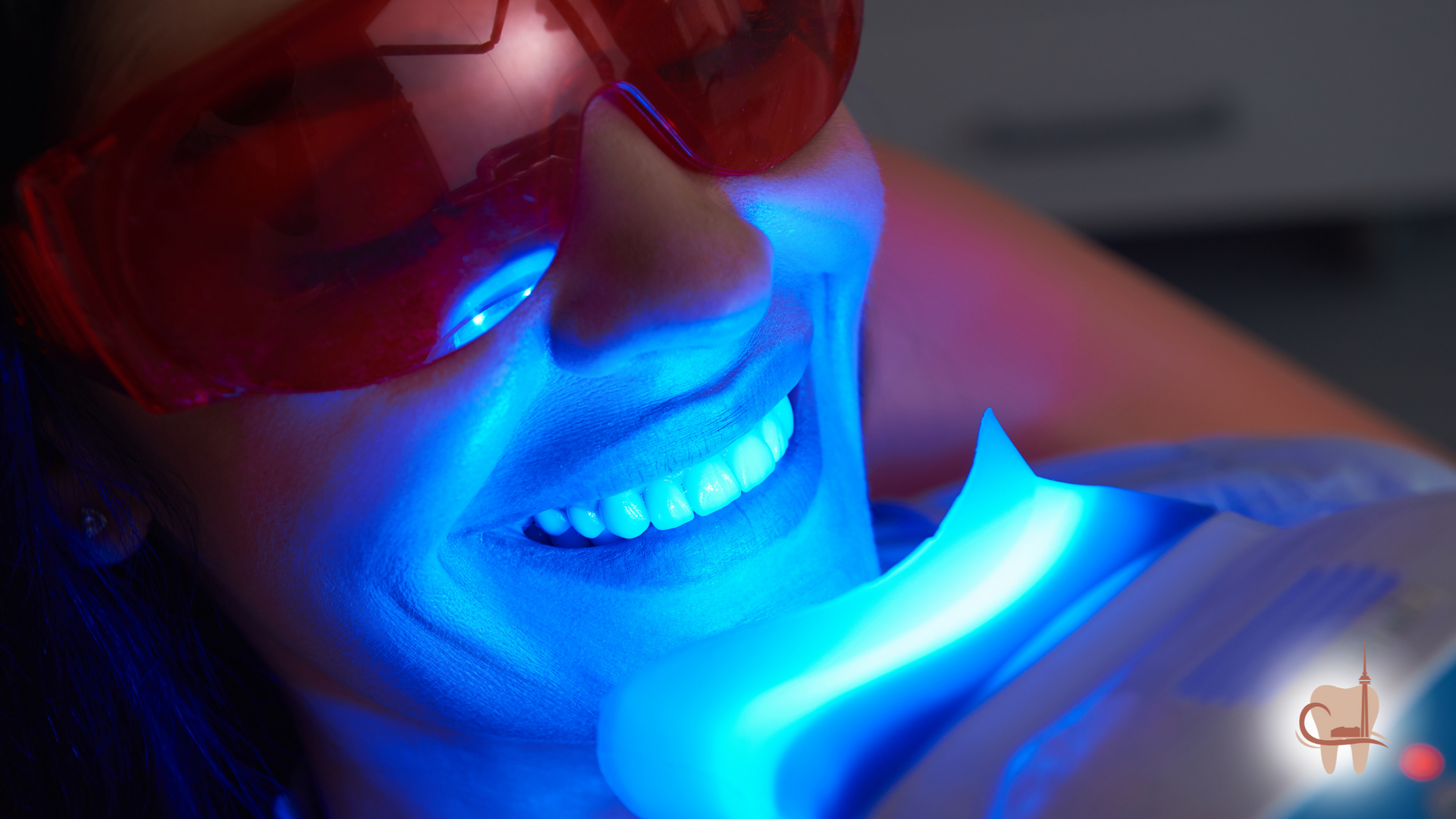 Woman undergoing professional teeth whitening with blue light. Wearing protective red glasses and smiling.