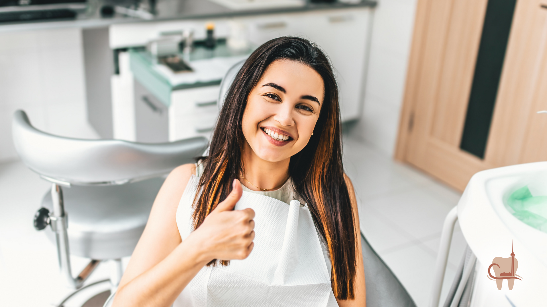 Woman in a dentist's chair gives a thumbs up, smiling. White dental office setting.