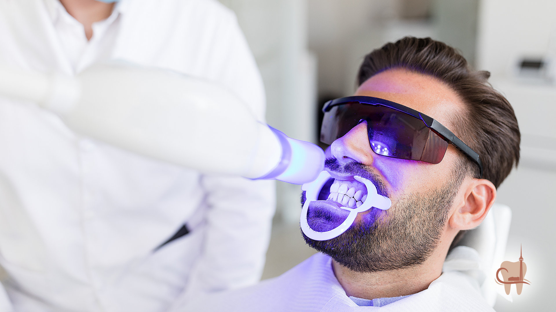 Man undergoing teeth whitening procedure at a dentist's office with protective eyewear.
