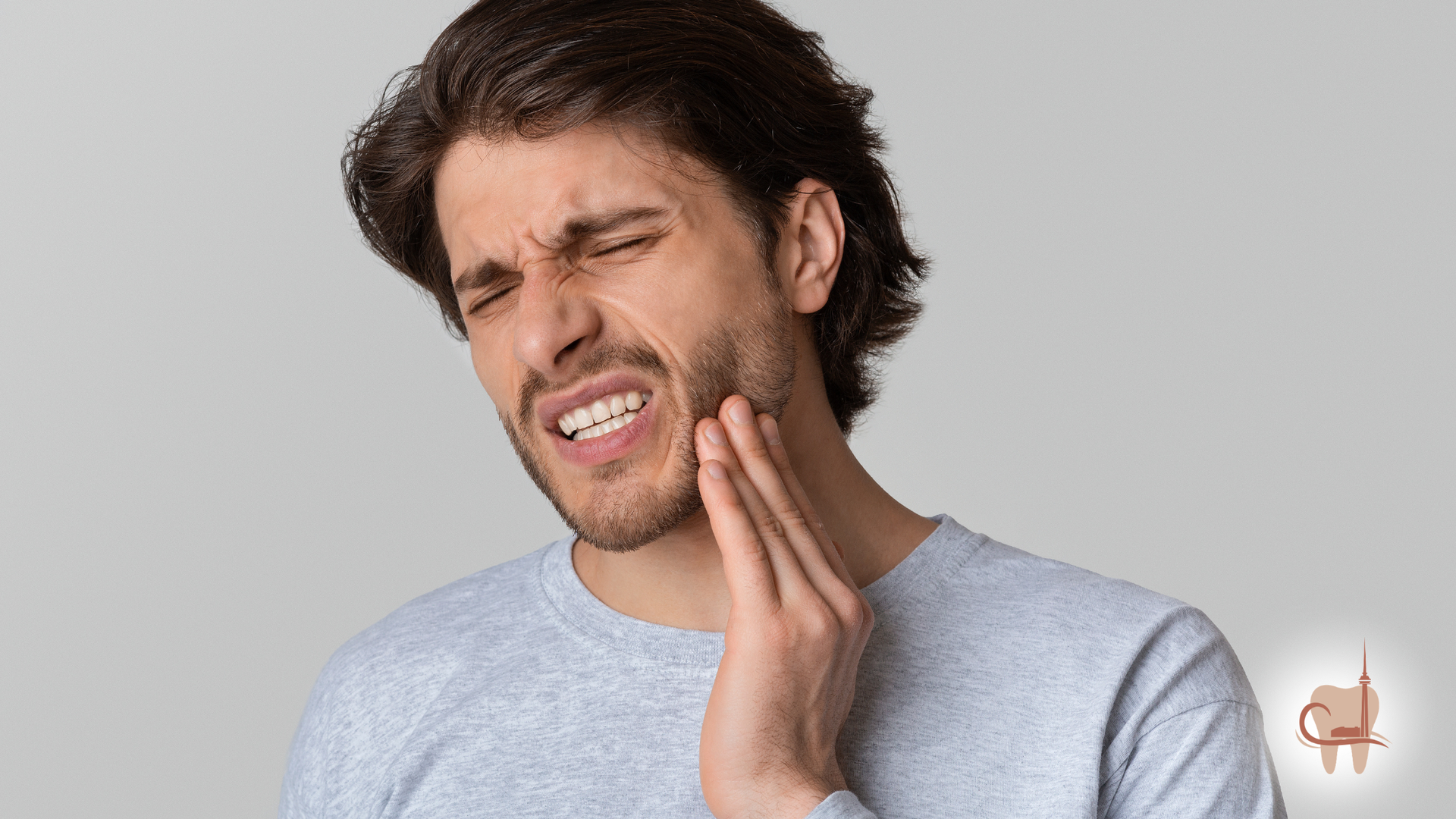 Woman holding face in pain, eyes closed, white tank top, light background.
