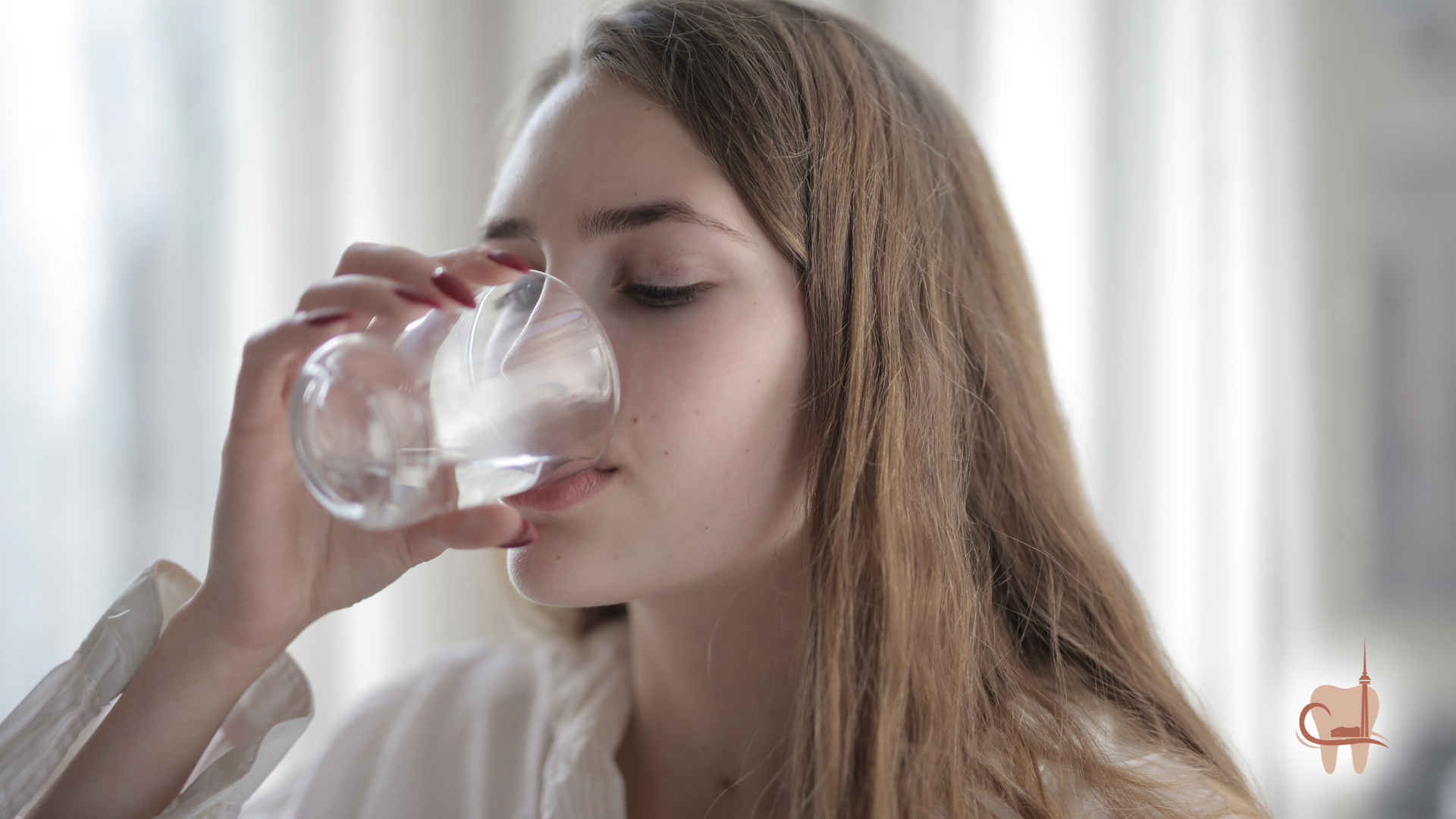 Woman drinking water from a clear glass in a bright, indoor setting.