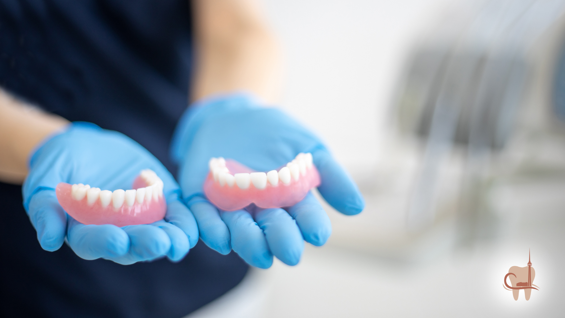 Hands in blue gloves holding two sets of dentures.
