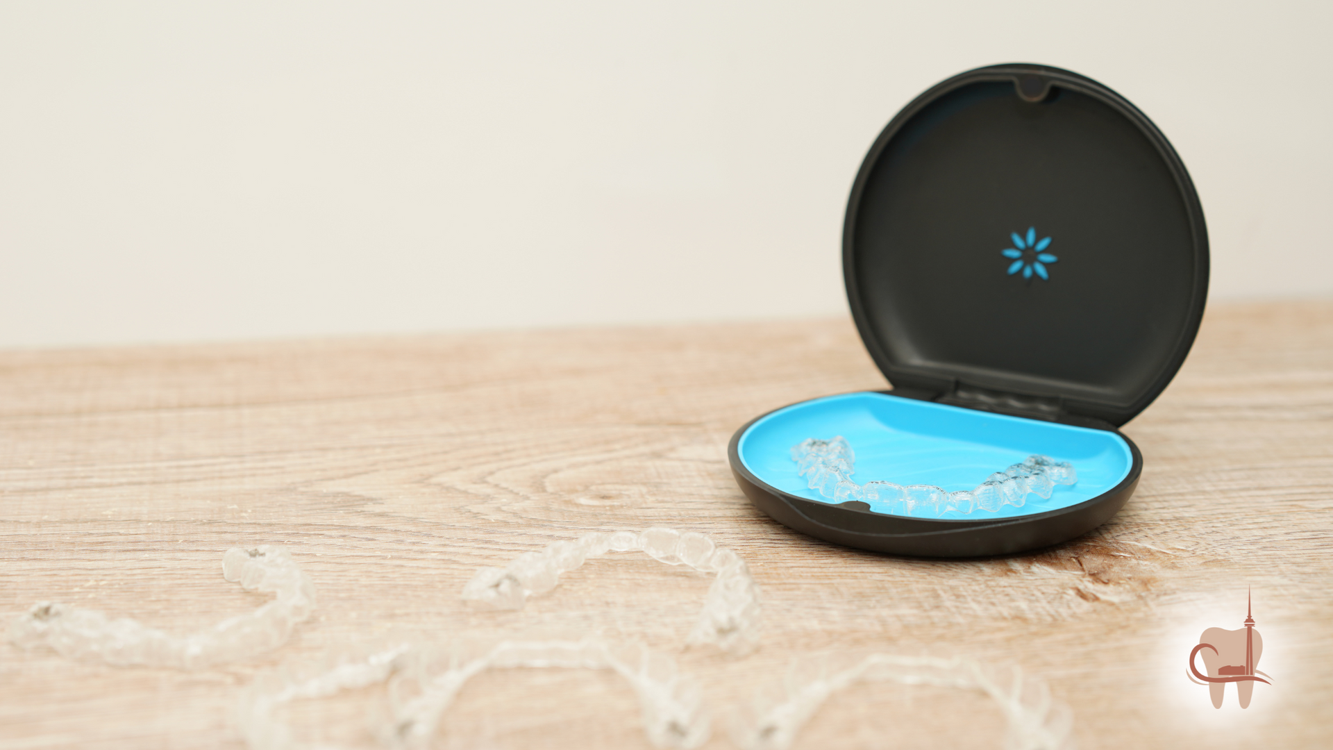 Invisalign aligners in a blue and black case on a wooden surface, with a few aligners scattered in front.