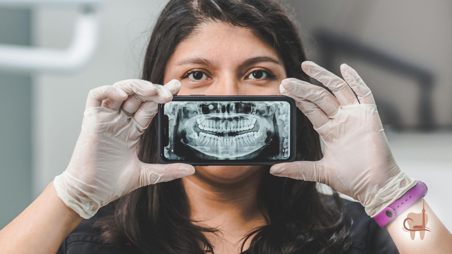 Woman in gloves holding a phone with a dental X-ray in front of her face.