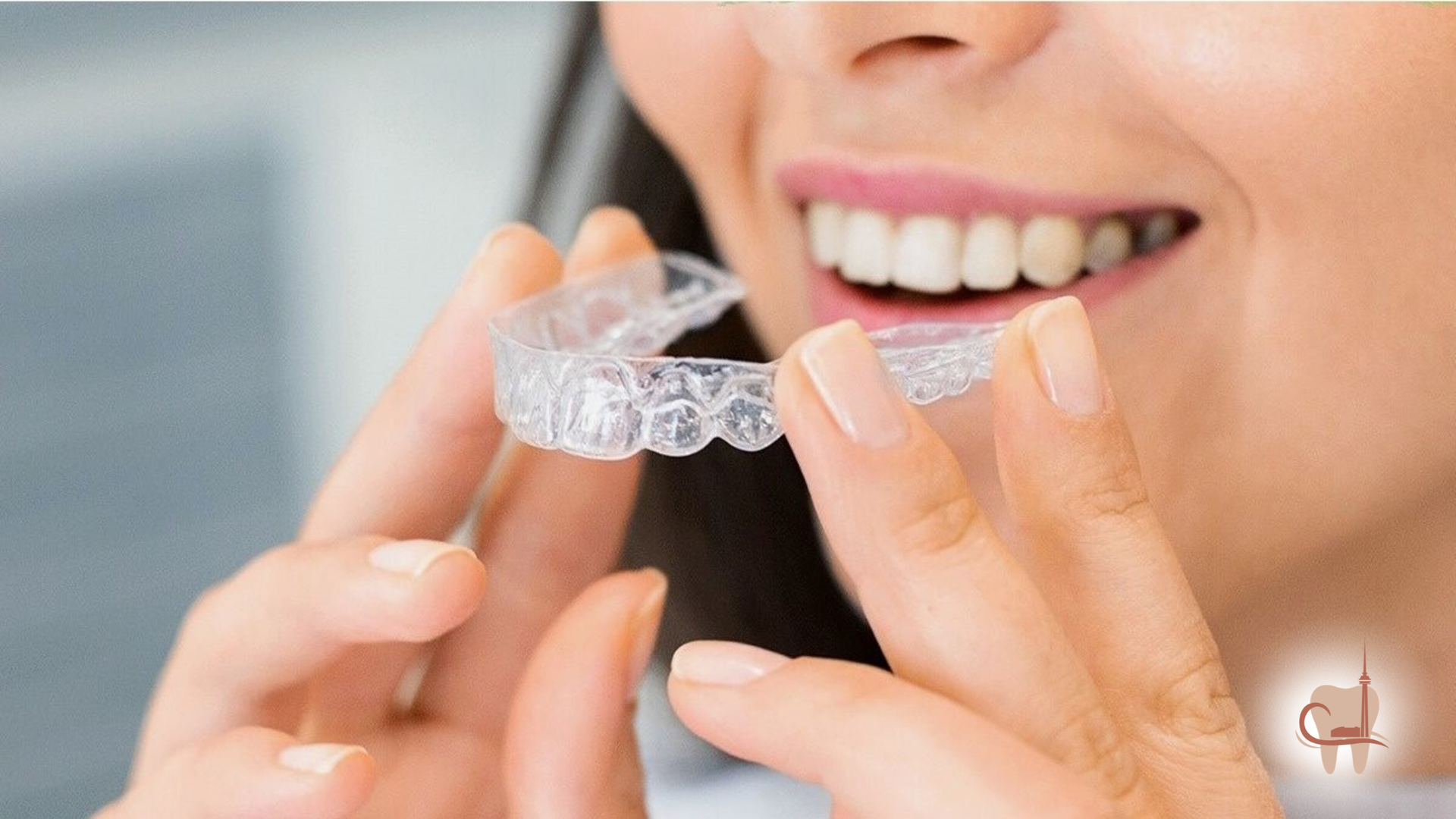 Person holding clear aligner, smiling, preparing to put it in mouth.