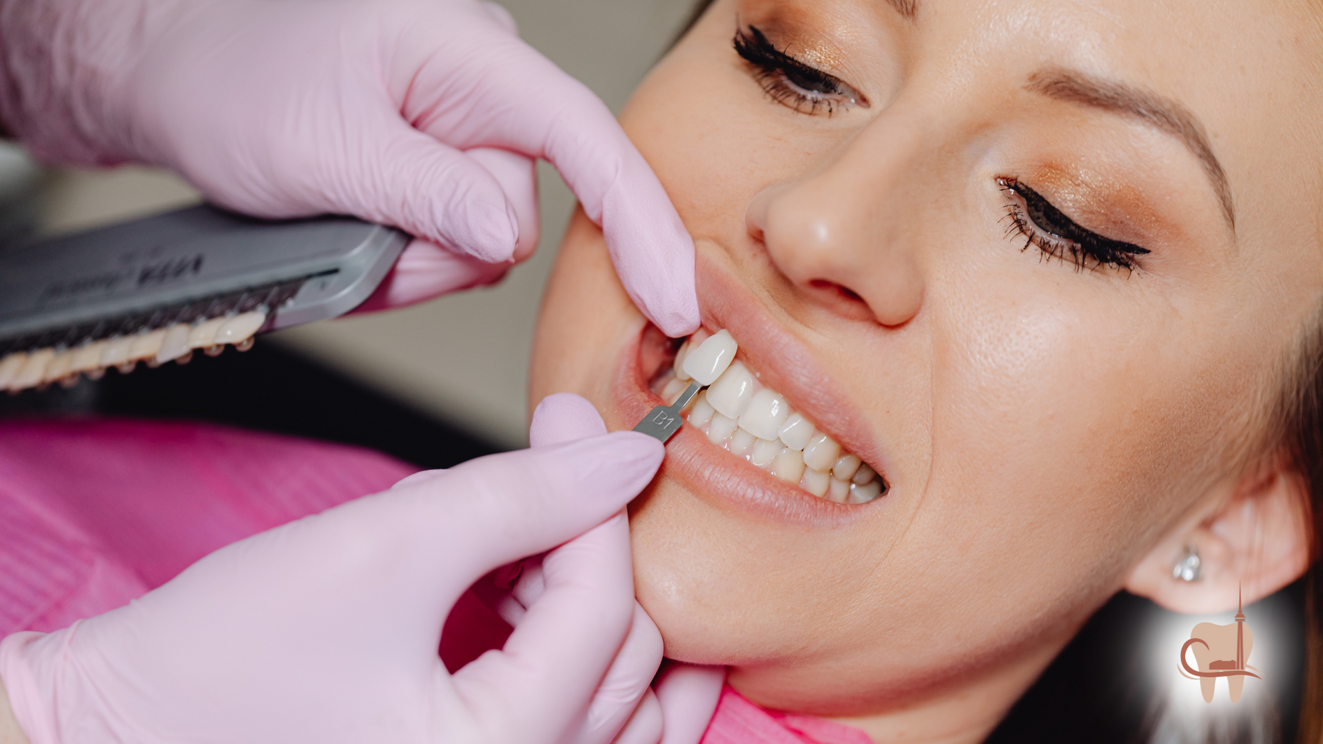 Dentist comparing tooth shade with a shade guide on a woman's teeth, pink gloves.