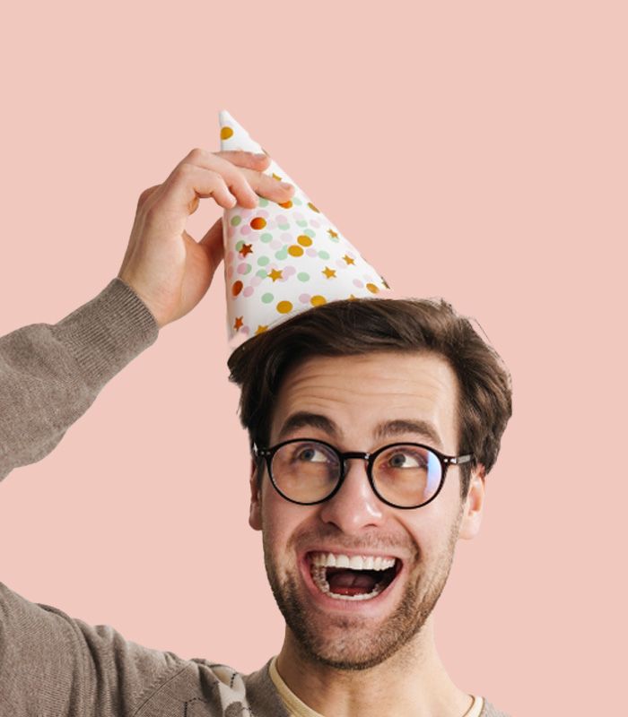 A man wearing glasses and a birthday party hat is smiling
