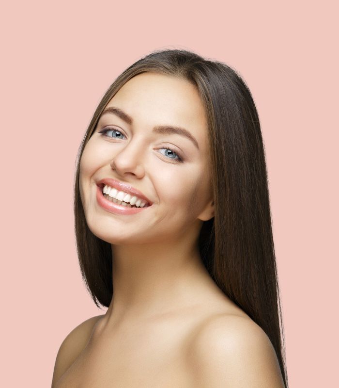 A woman with long hair is smiling on a pink background.
