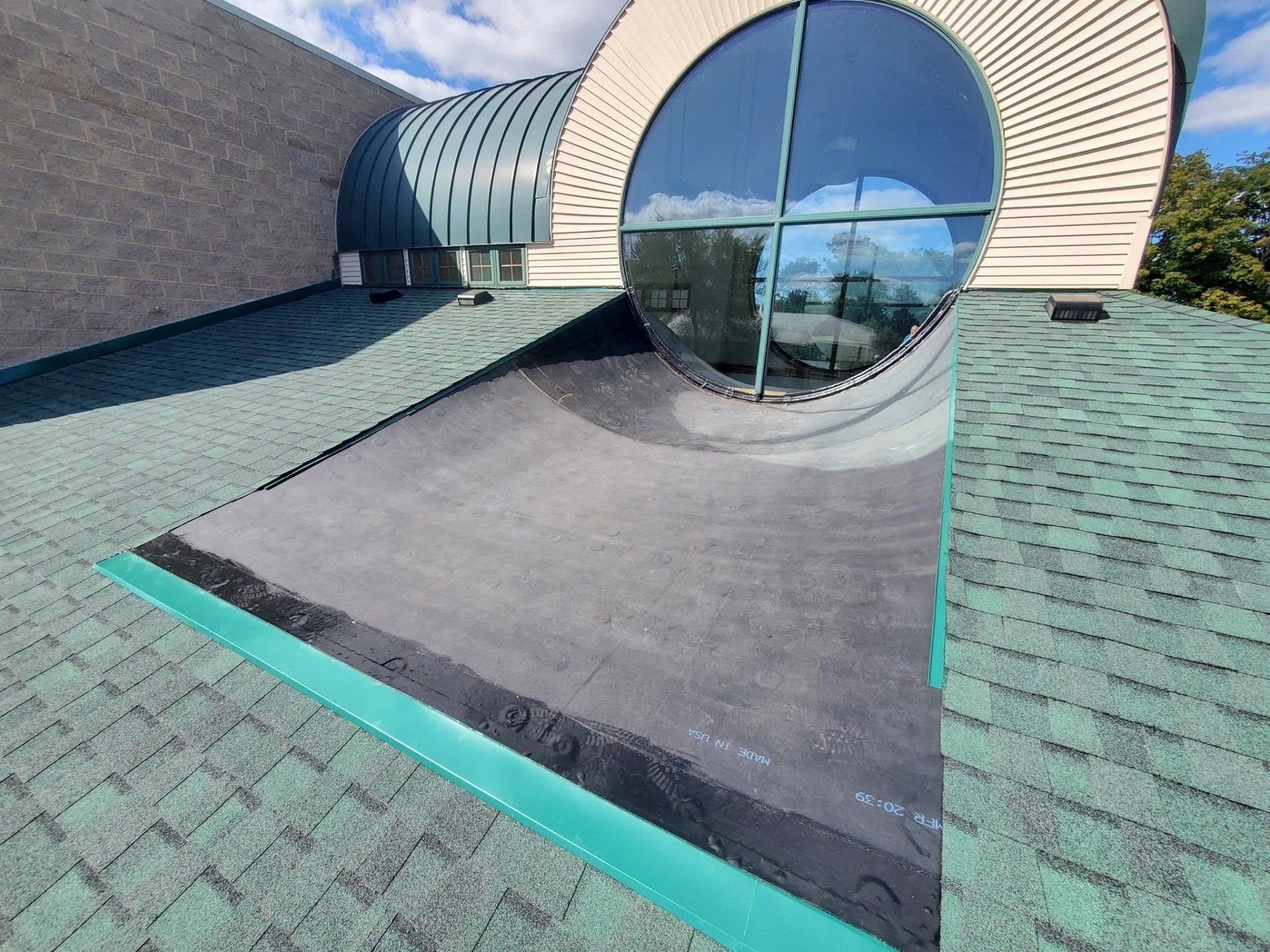 Green-shingled roof with a circular window and curved metal roof section.