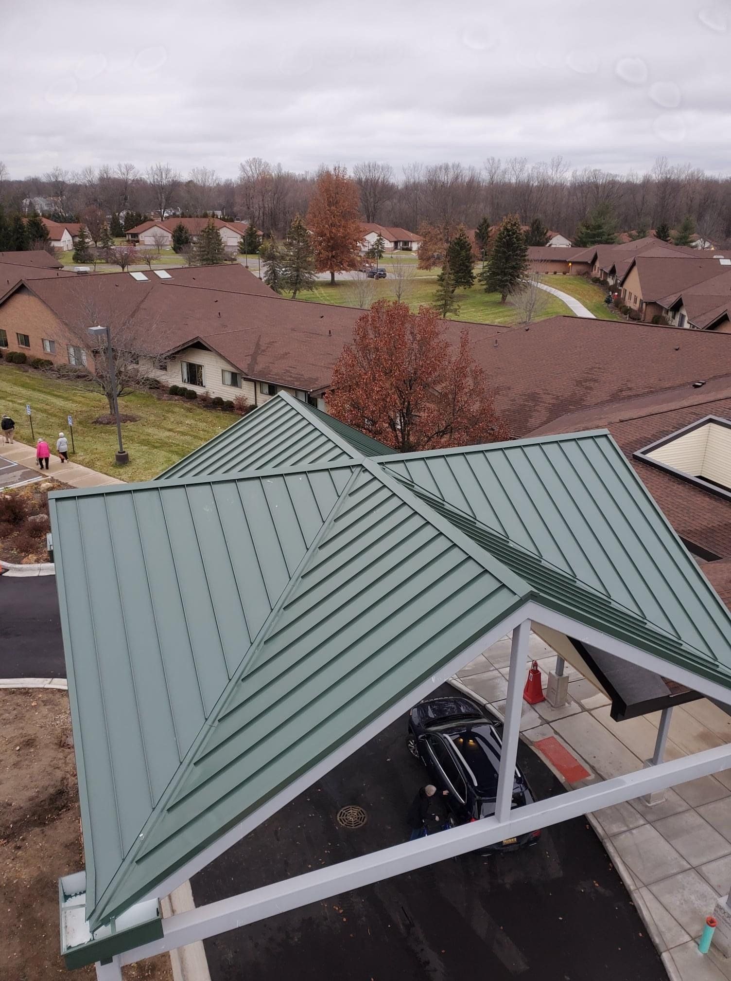 Green metal roofed carport with a view of buildings and trees under a cloudy sky.