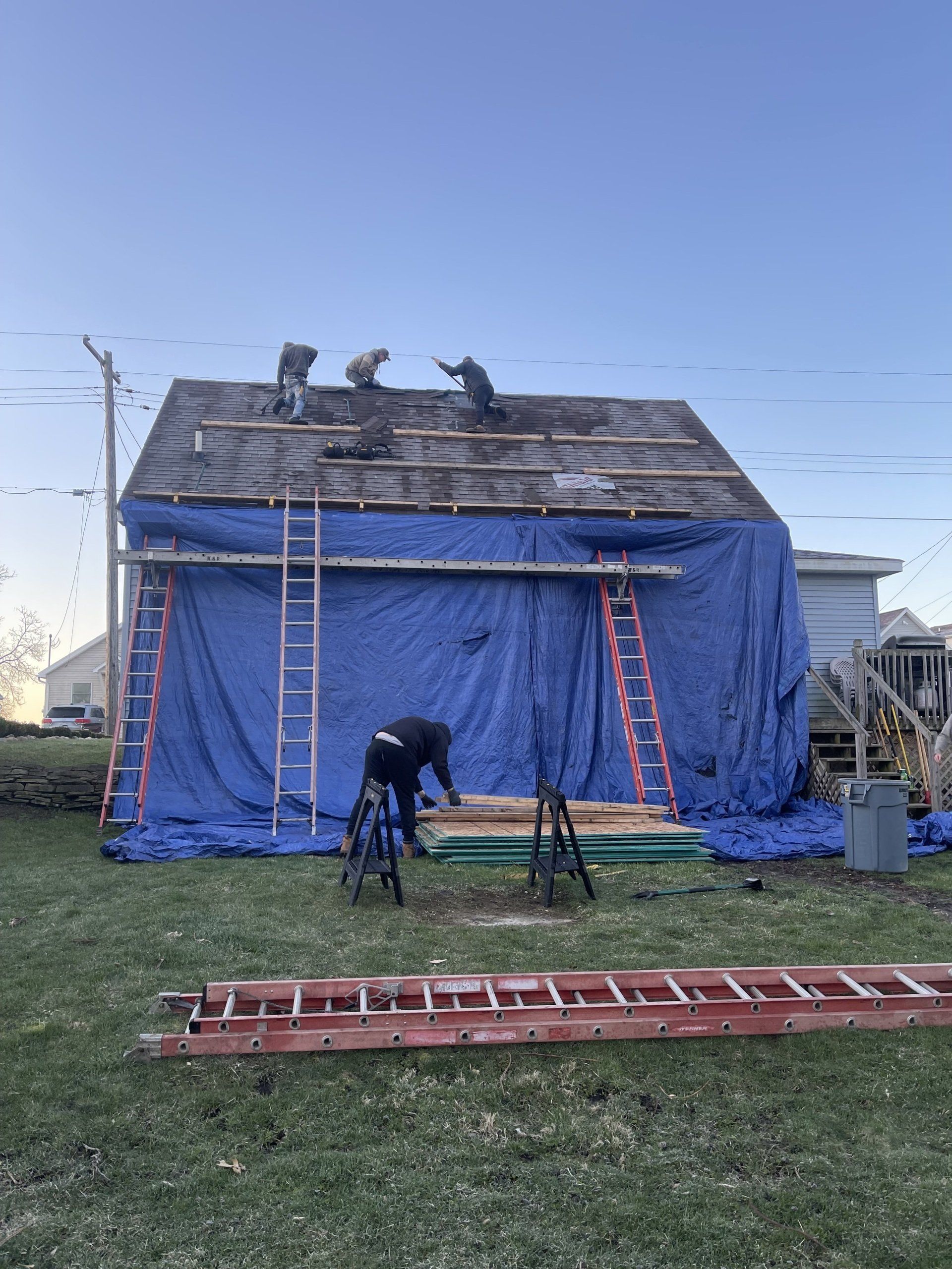 Roof repair in progress: Workers on a house with a blue tarp. Ladders and tools are present.