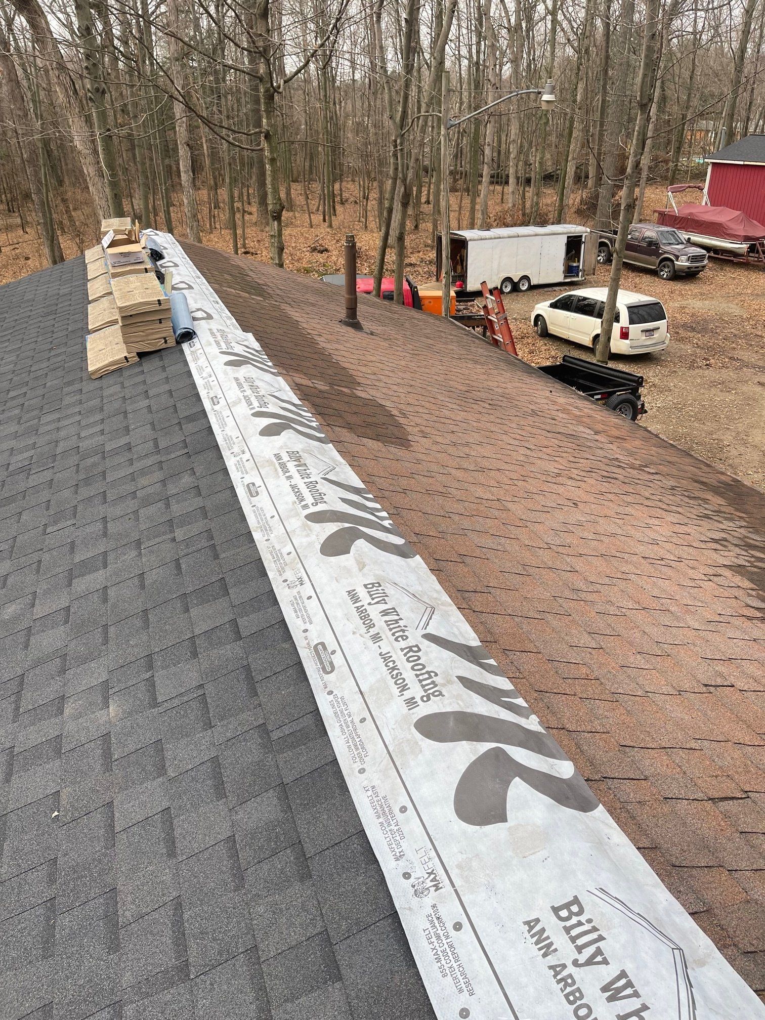 Rooftop with installed underlayment. Shingles, wood, and a vehicle are visible in the outdoor setting.