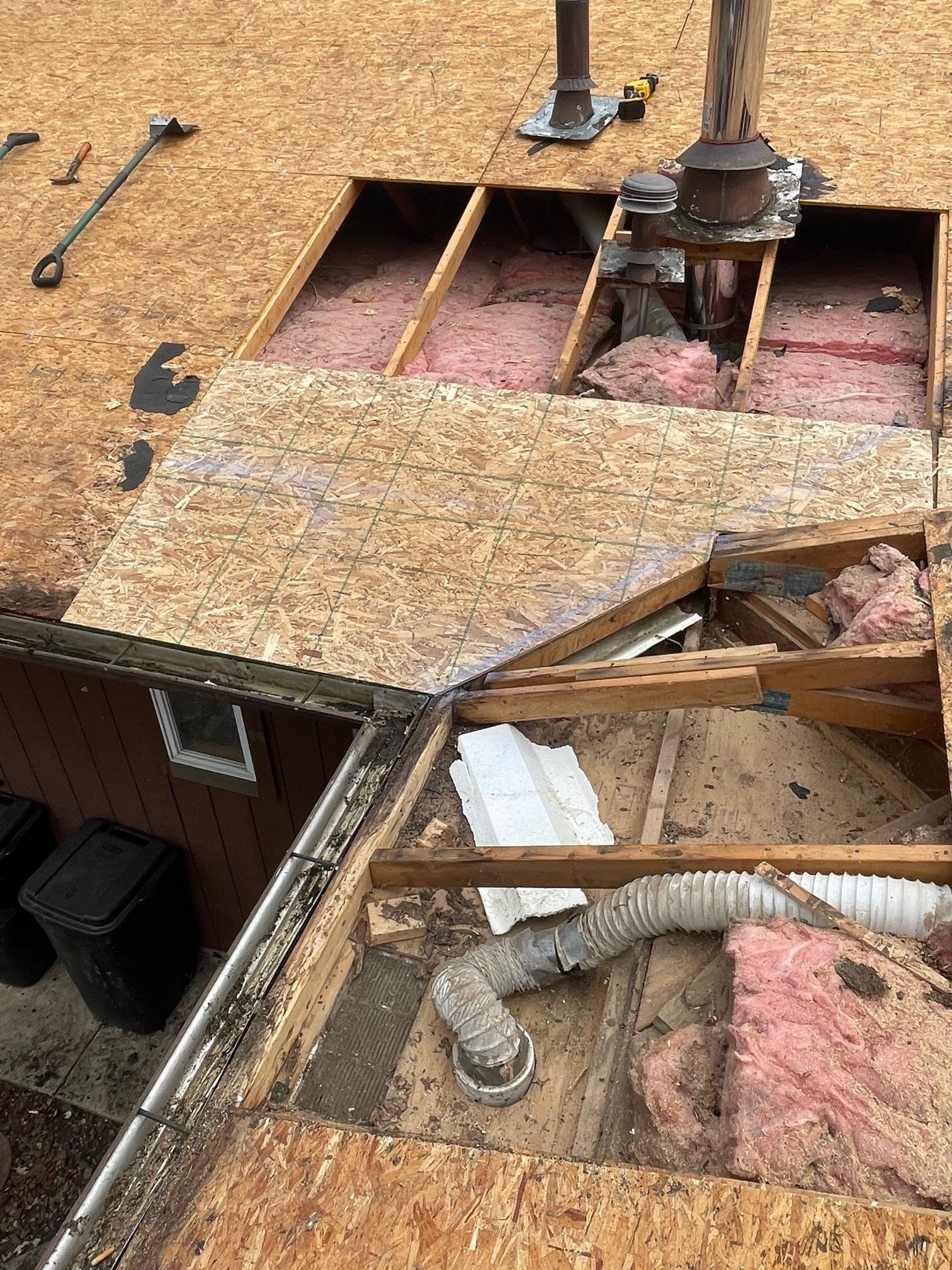 Rooftop with removed sections, showing plywood, framing, insulation, and chimney elements.