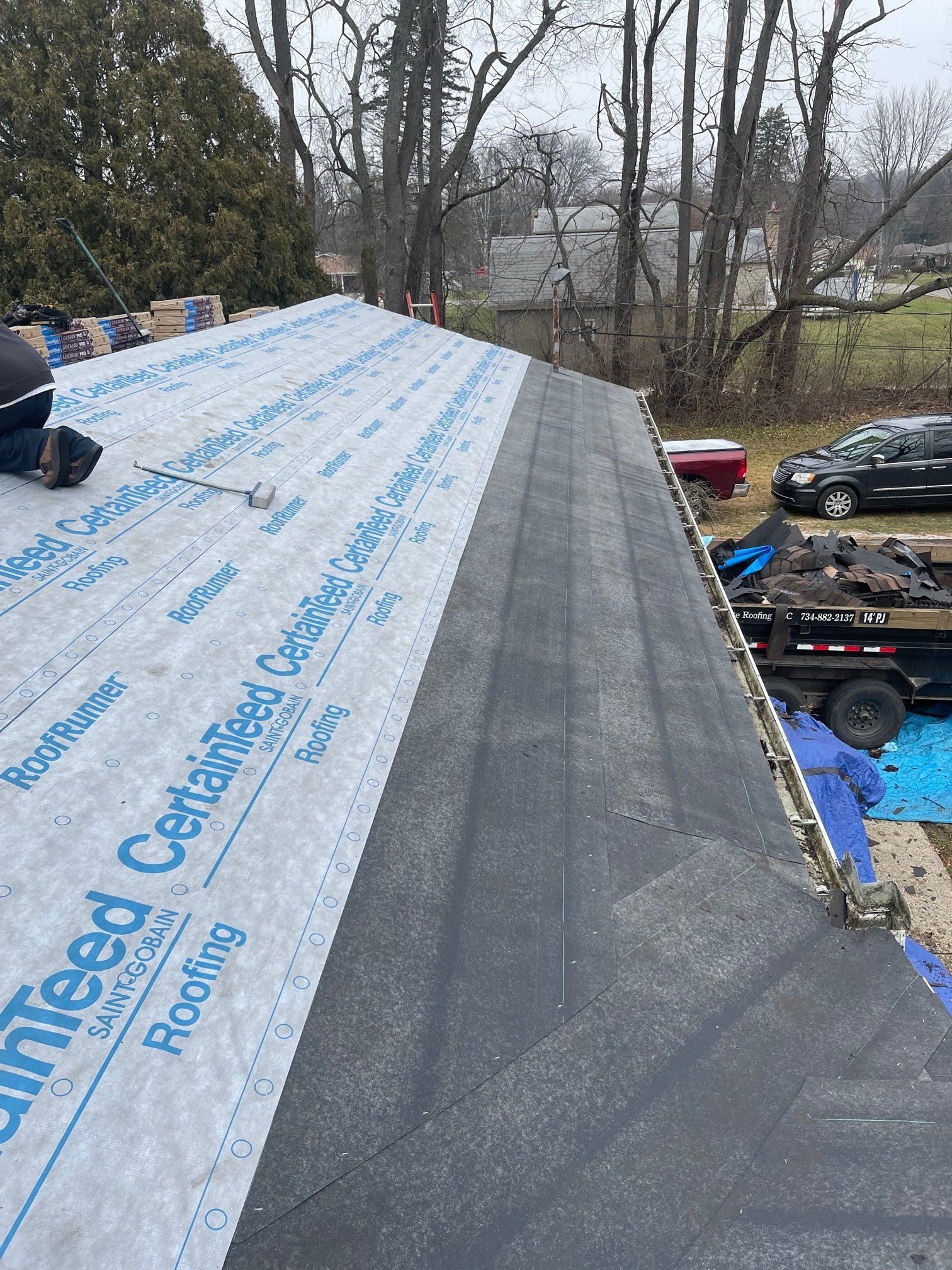 Roofers installing asphalt shingles on a house roof. Blue underlayment and debris visible.