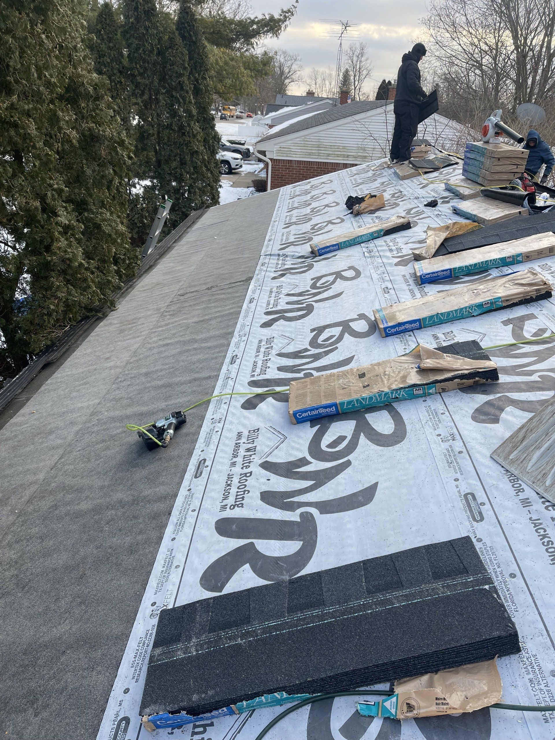 Roofers working on a residential roof, laying down underlayment and shingles. Snowy day.