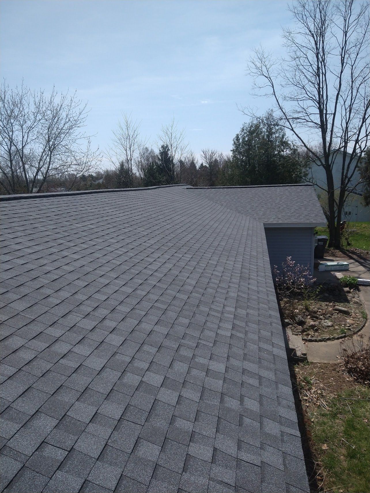 Gray shingled roof under a clear blue sky. Trees in the background.