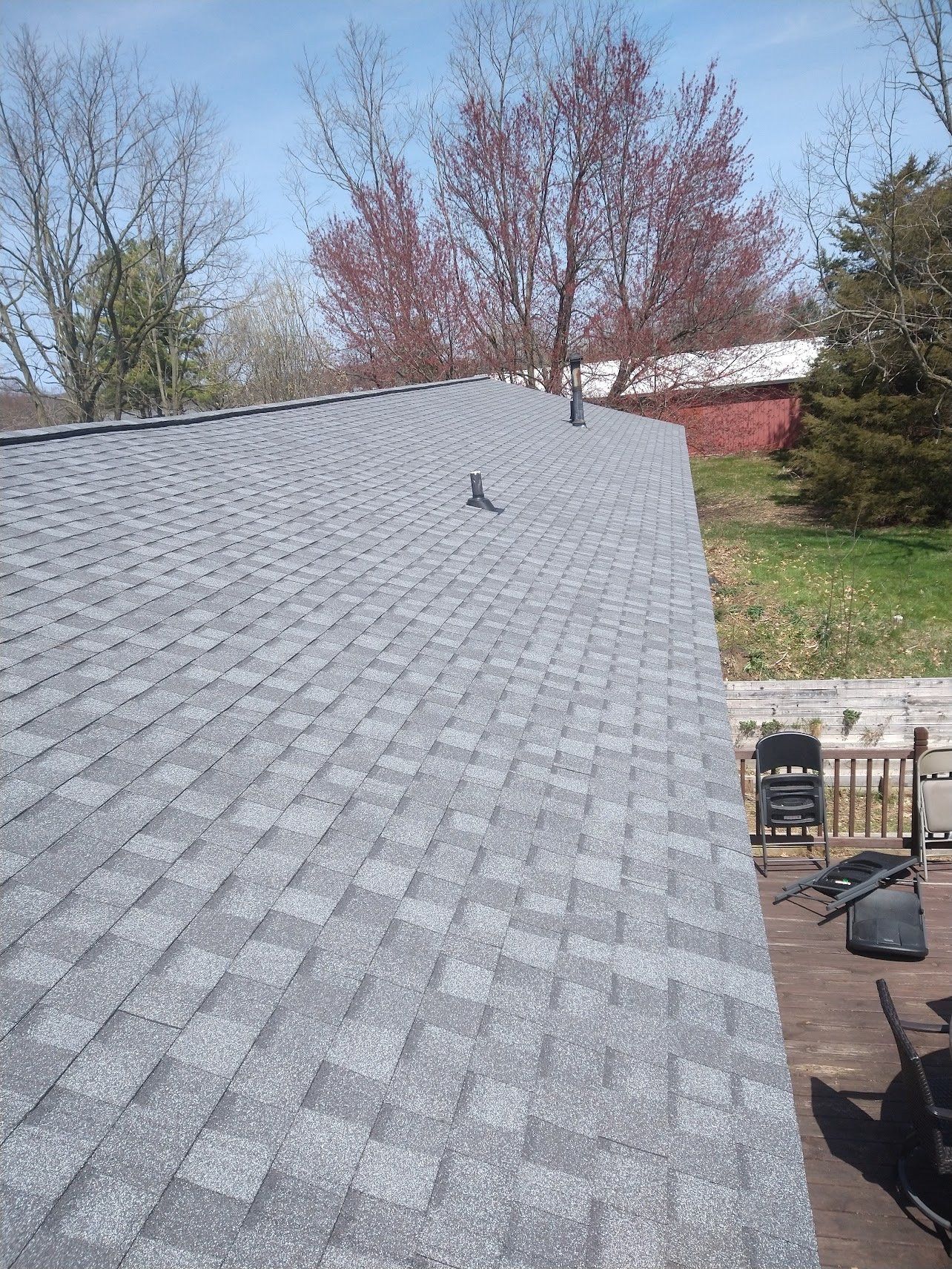 Gray asphalt shingle roof on a sunny day with trees and part of a deck visible.