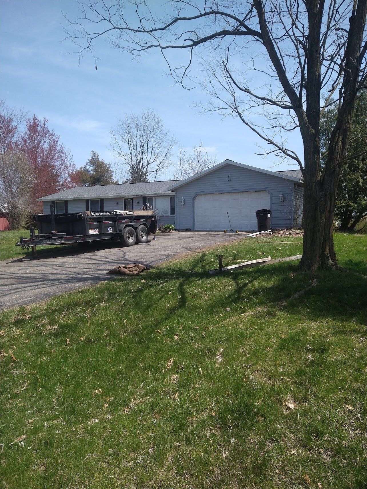Ranch style house with attached garage. Trailer parked in driveway. Sunny day.