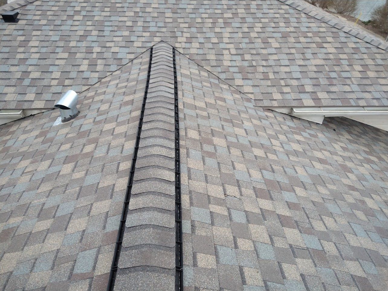 View of a roof with brown and grey asphalt shingles and a metal flashing.